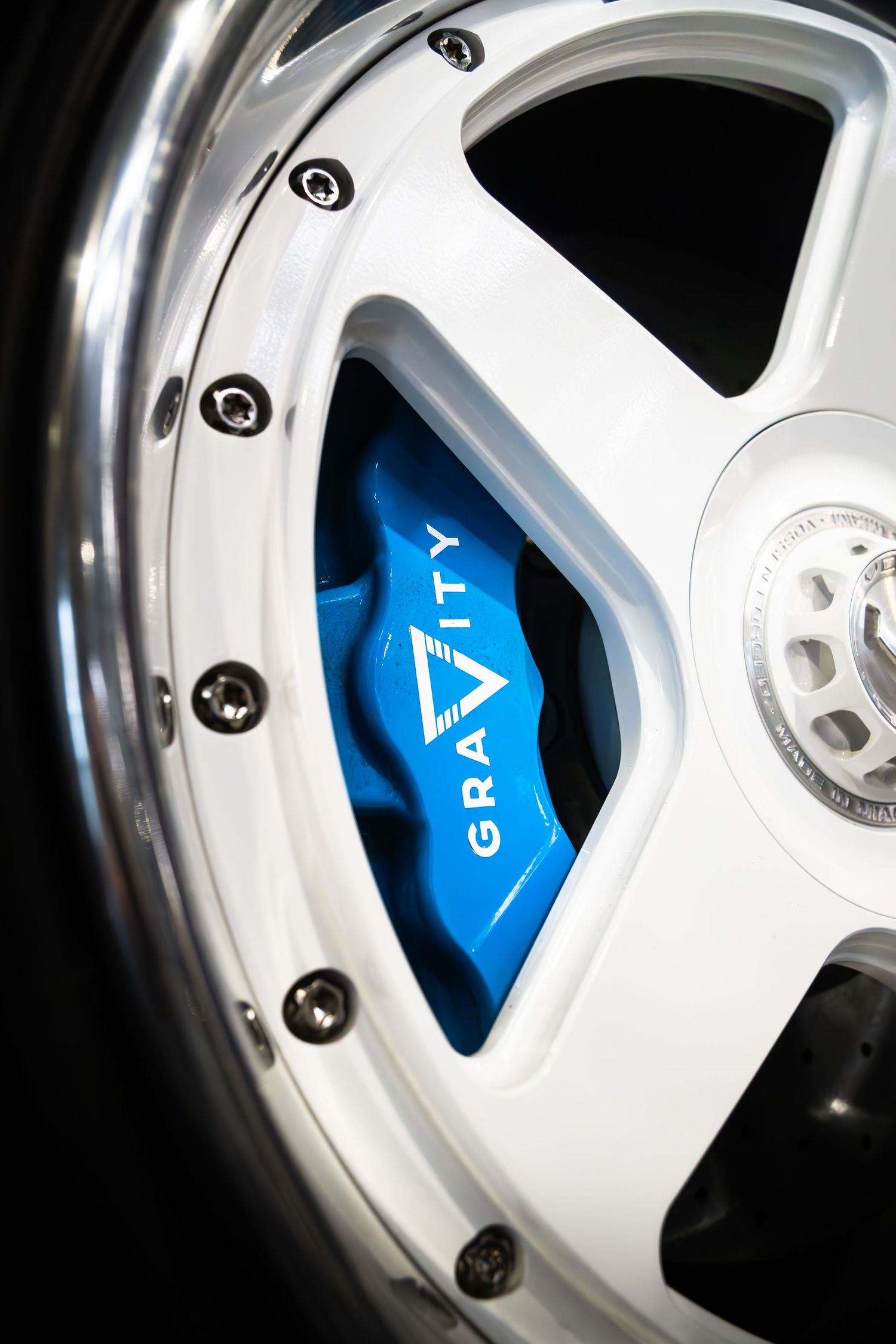 Close-up of a white multi-spoke alloy wheel with blue Gravity branded brake caliper.