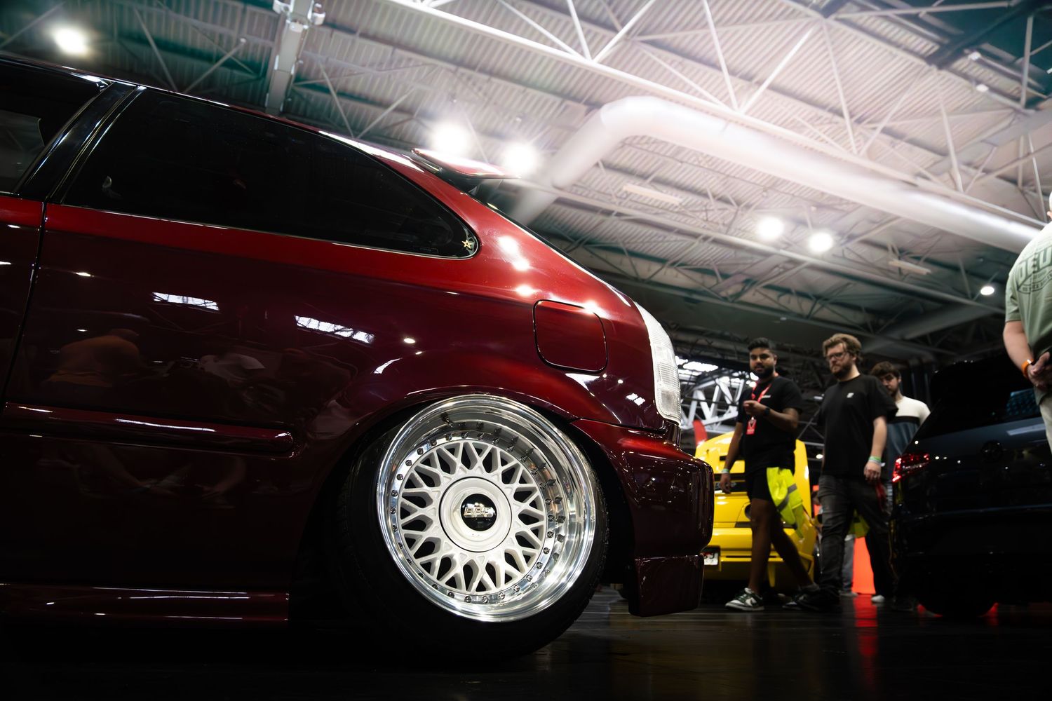 Deep red lowered car with polished BBS mesh wheels on display at indoor car show.
