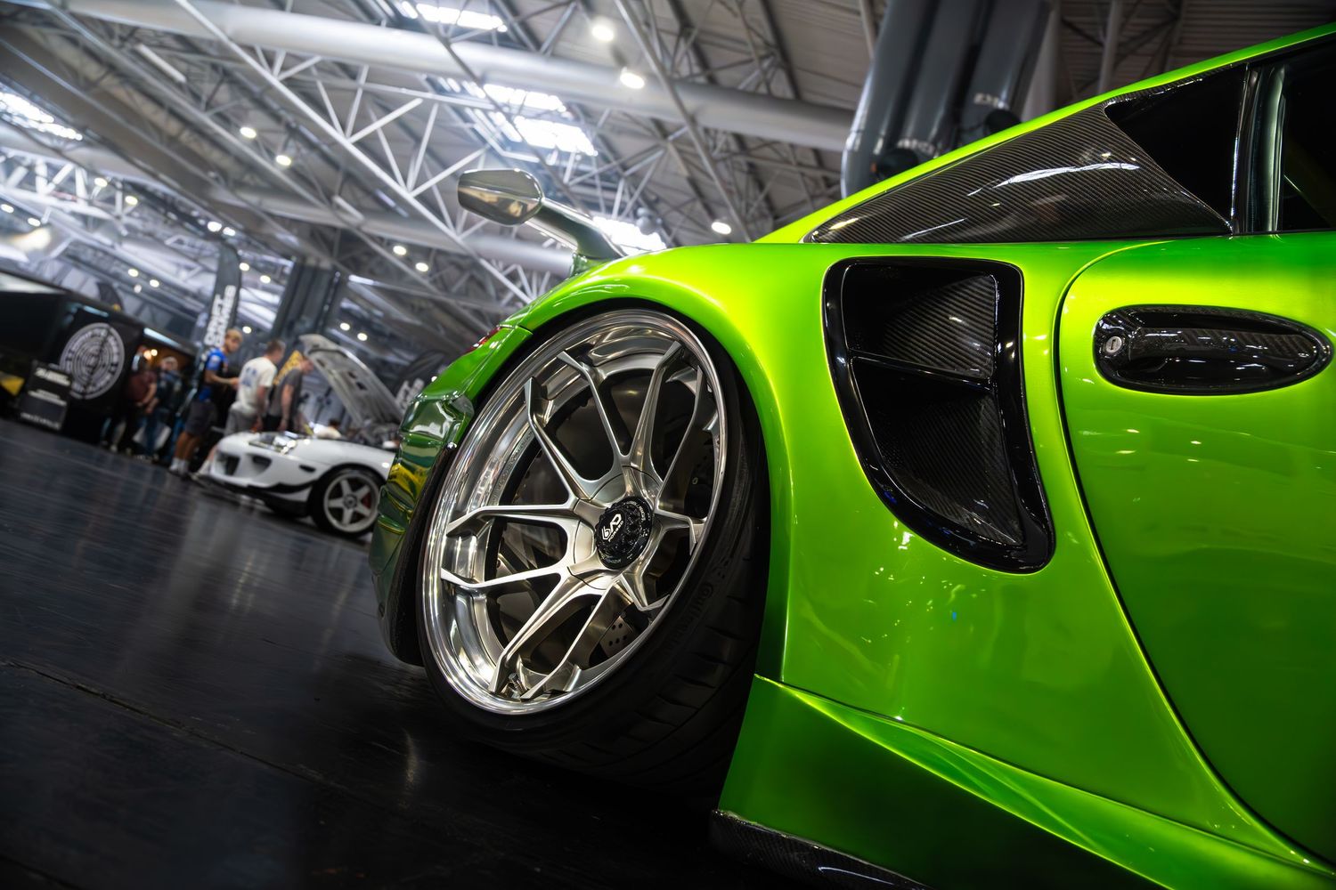 Close-up of a lime green Porsche 911 with chrome wheels at an auto show.