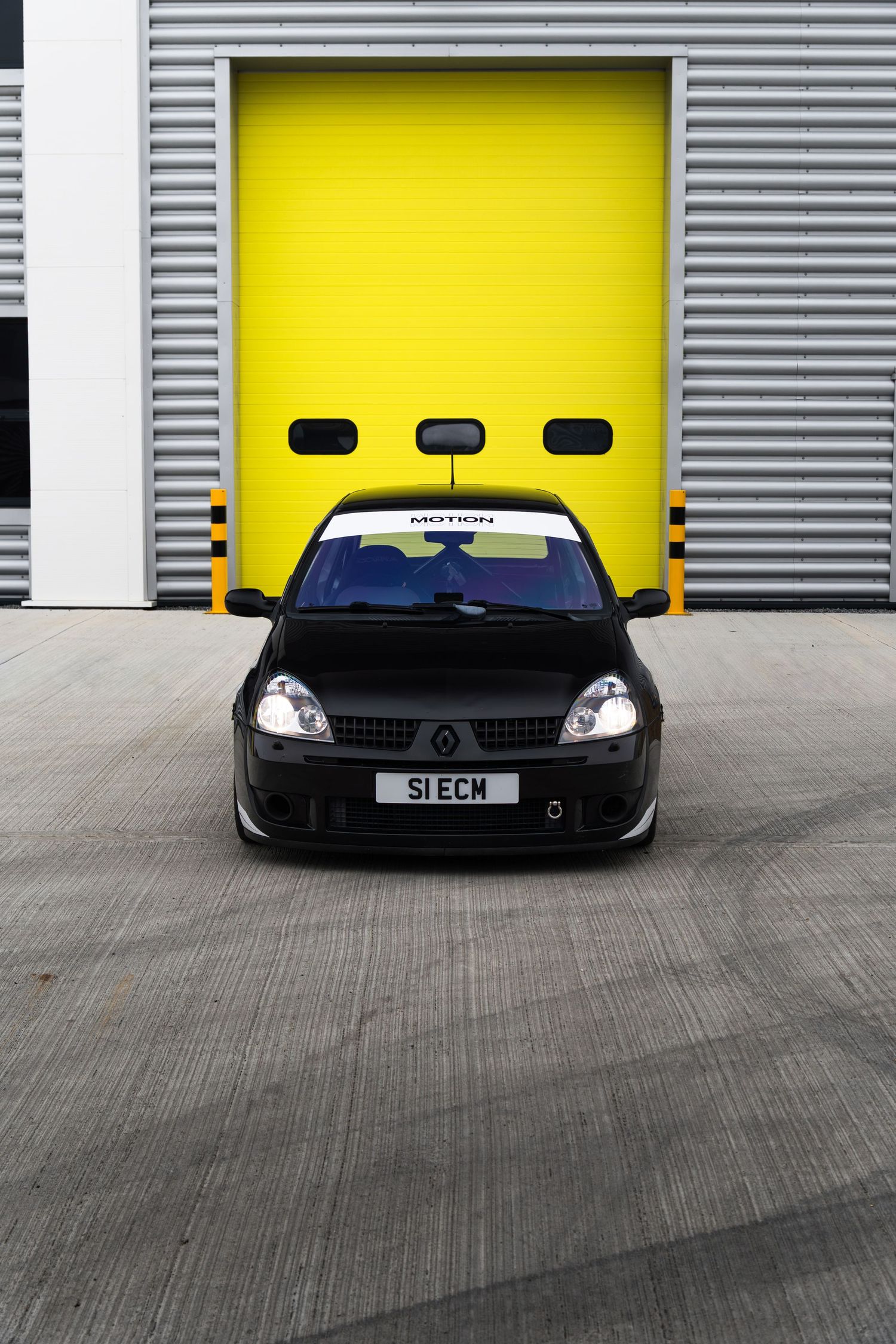 Black Renault Clio with Motion banner photographed head-on in front of bright yellow garage doors.