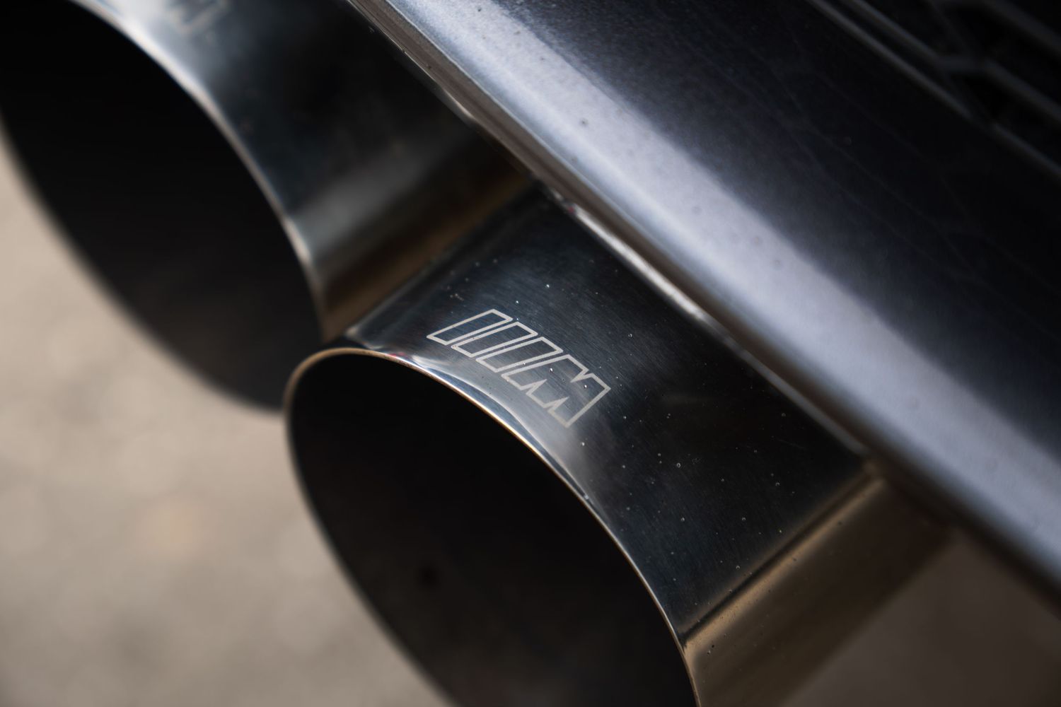Close-up of dual BMW M exhaust tips with embossed M logo on dark metal finish.