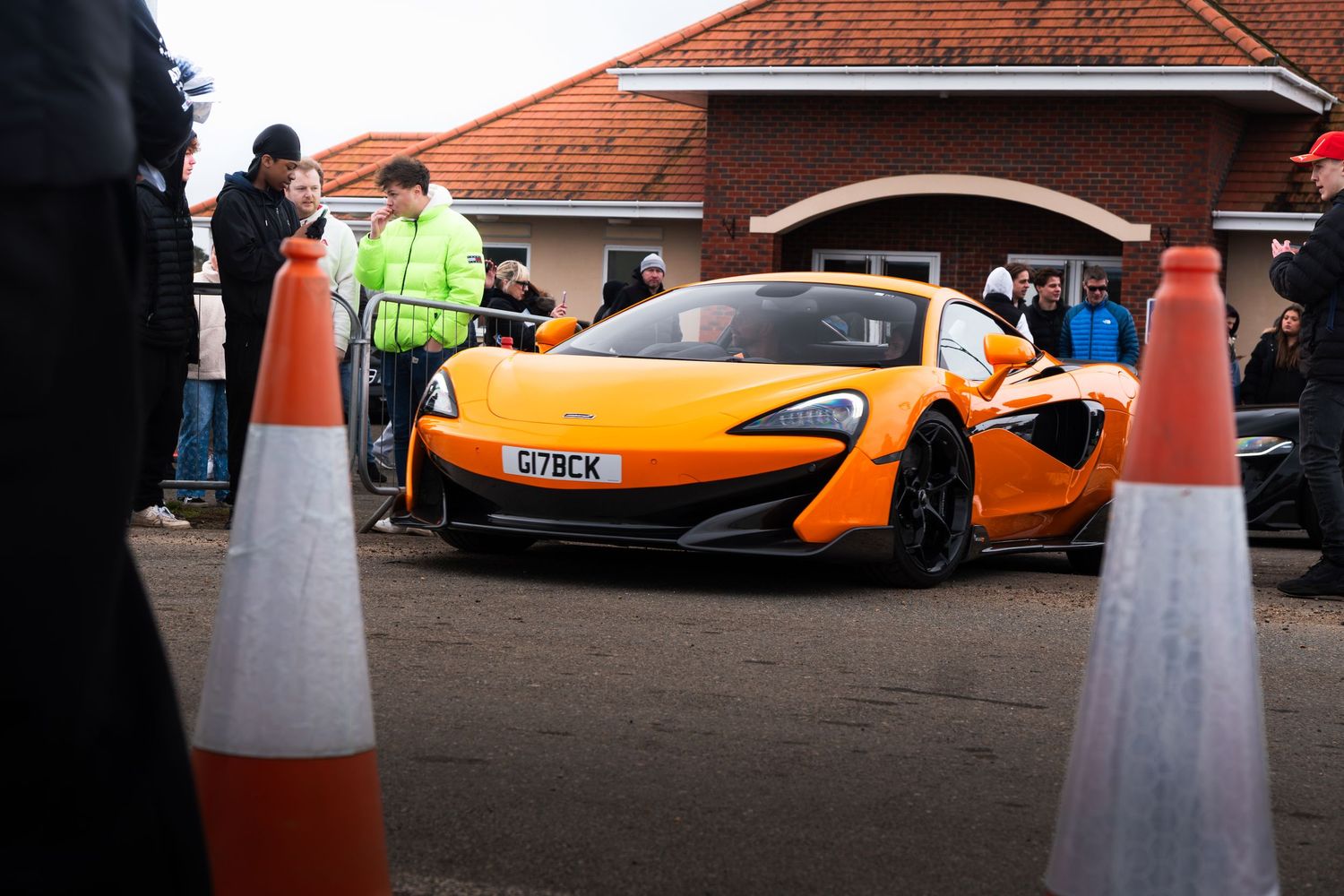Orange McLaren 570S supercar at a car meet event with orange traffic cones in foreground.