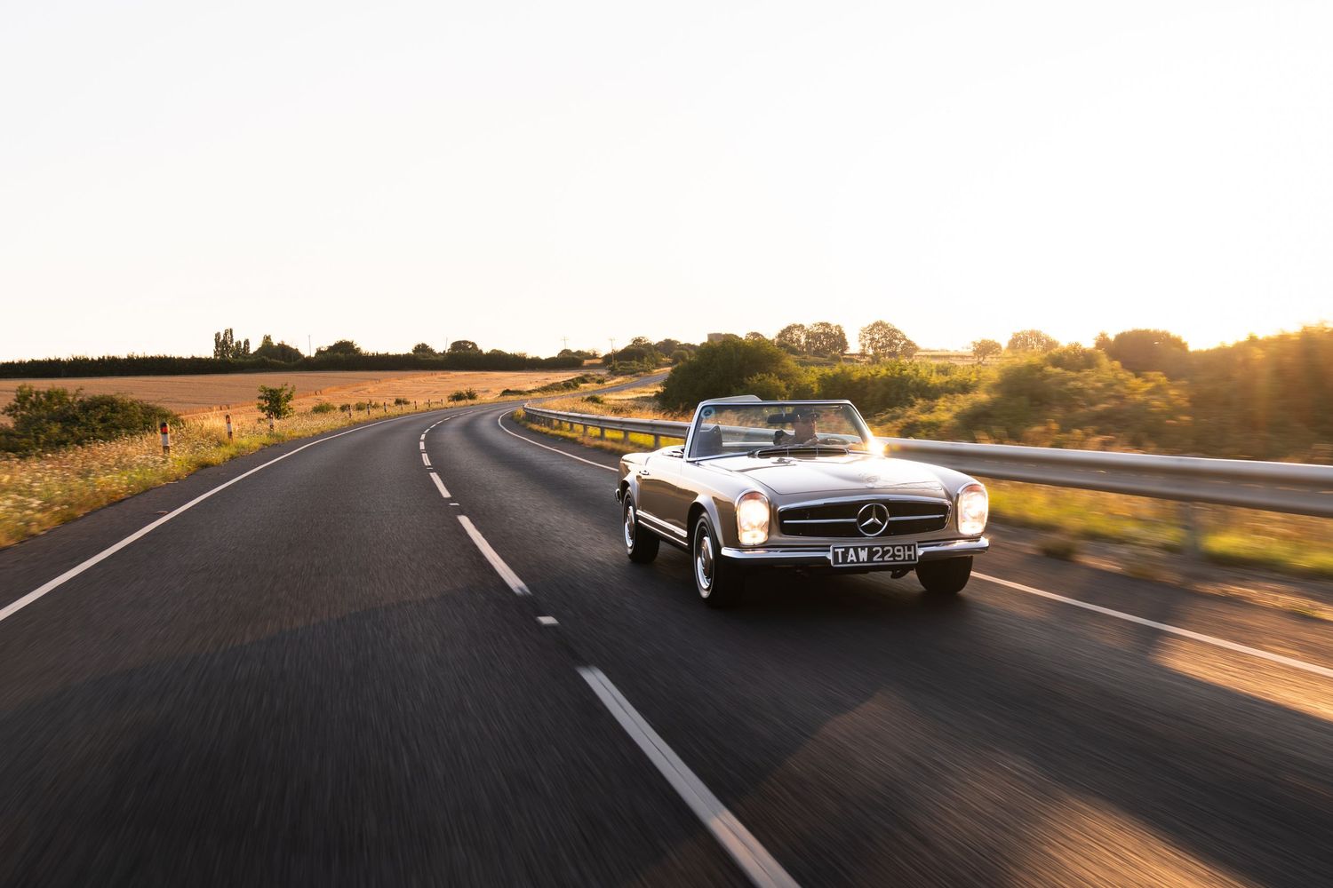 Classic white Mercedes-Benz convertible cruising on an open road at golden hour sunset.