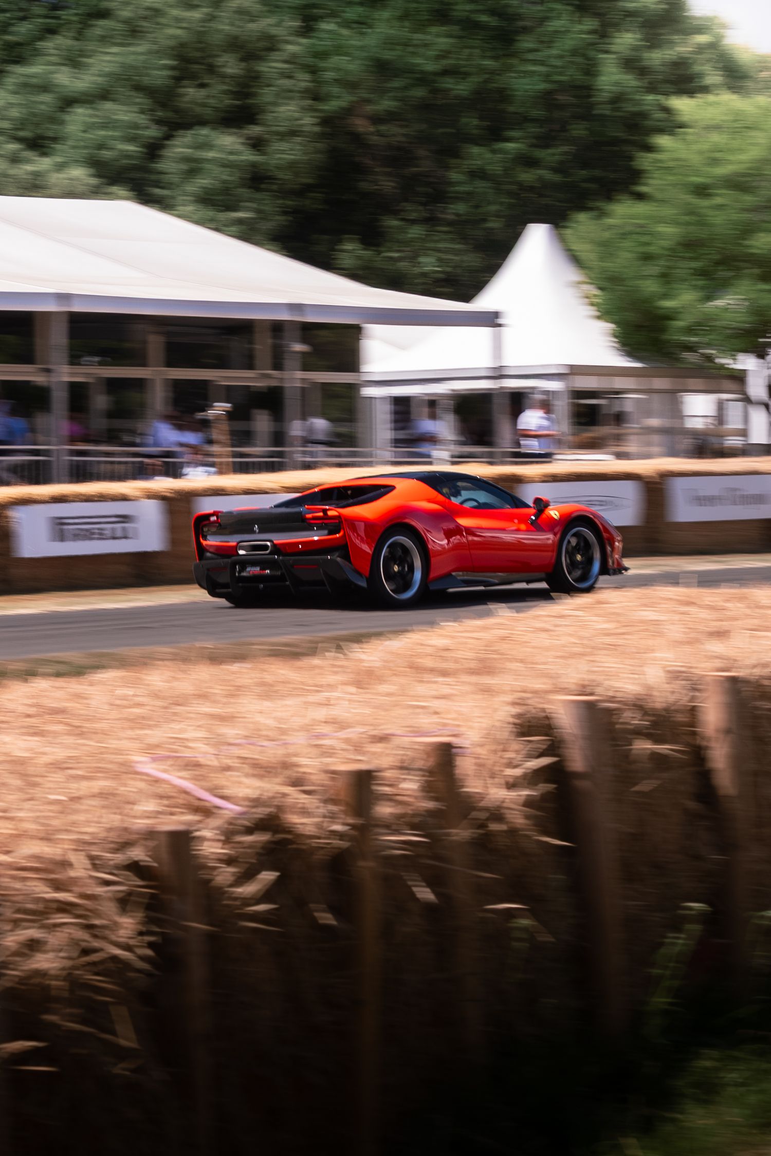 Red Ferrari supercar speeding past hay bales at Goodwood Festival of Speed hillclimb event.