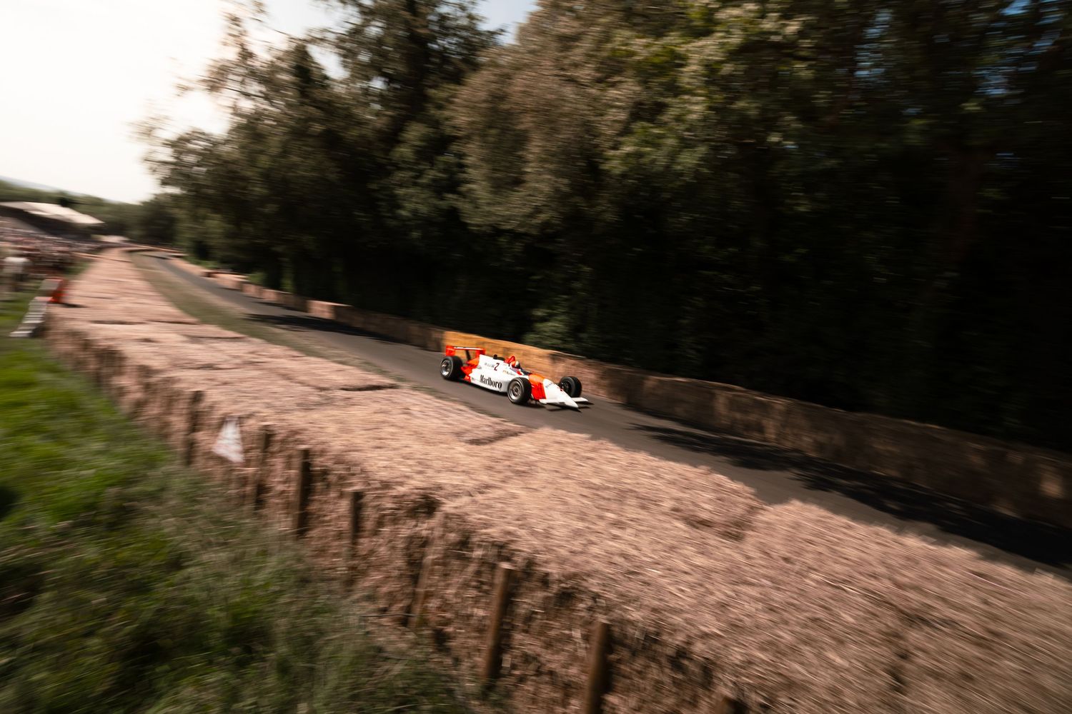 A white and orange Formula 1 racing car speeds along a tree-lined track during a vintage motorsport event.