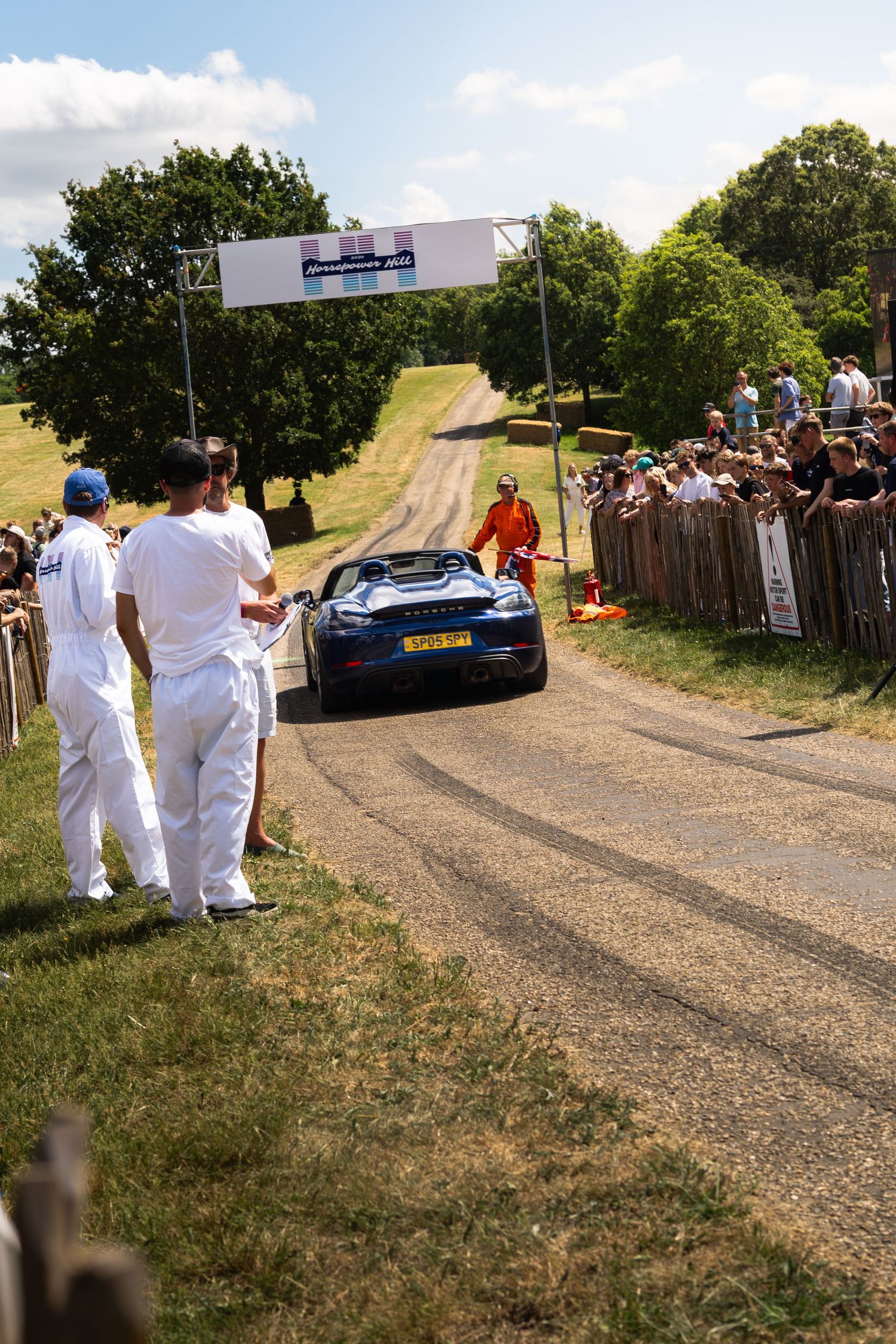 Blue sports car navigates a hillclimb course at Goodwood Festival of Speed, watched by crowds lining the track.