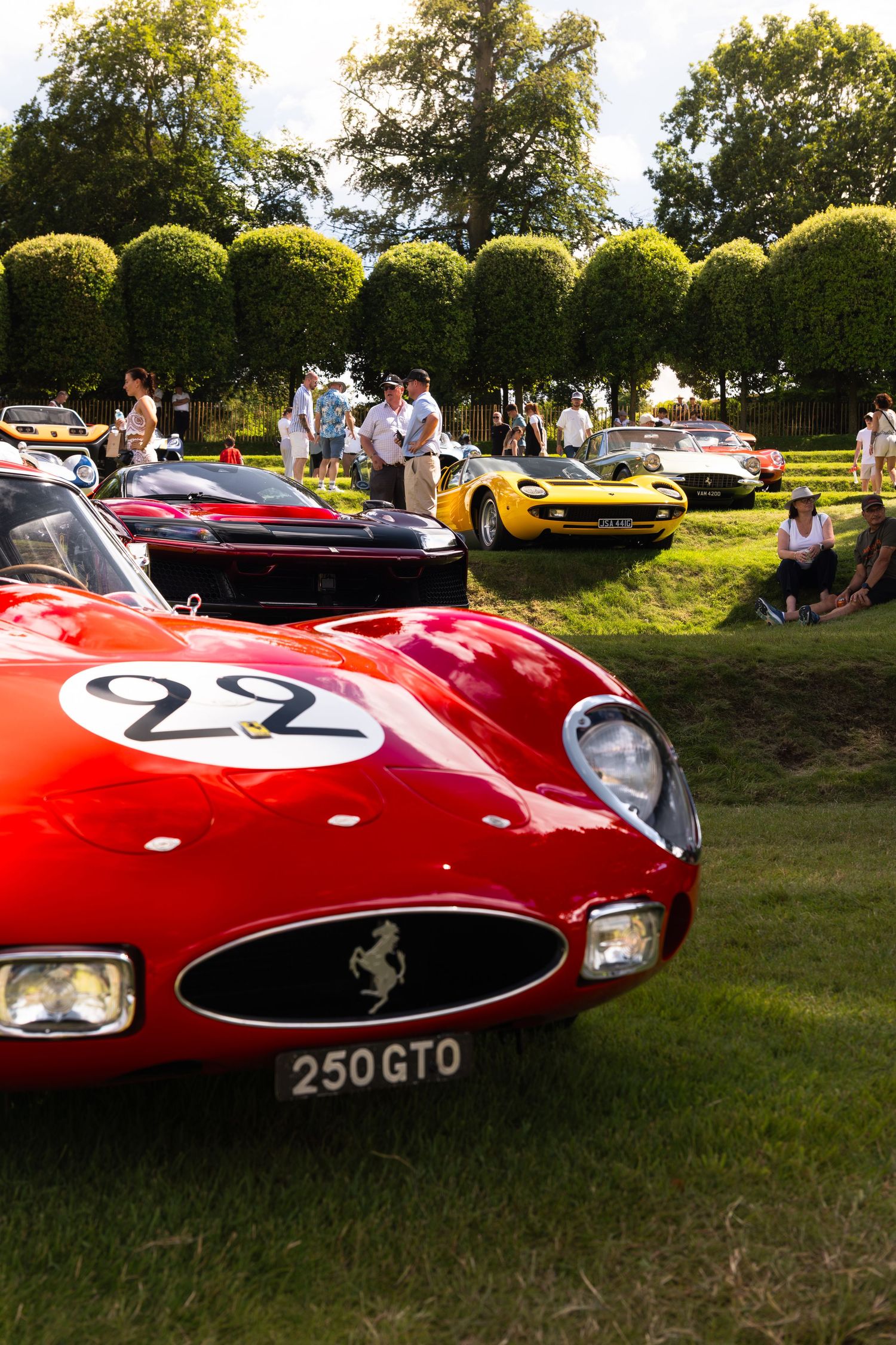 Red Ferrari 250 GTO race car with number 22 displayed at an outdoor classic car show on green grass.