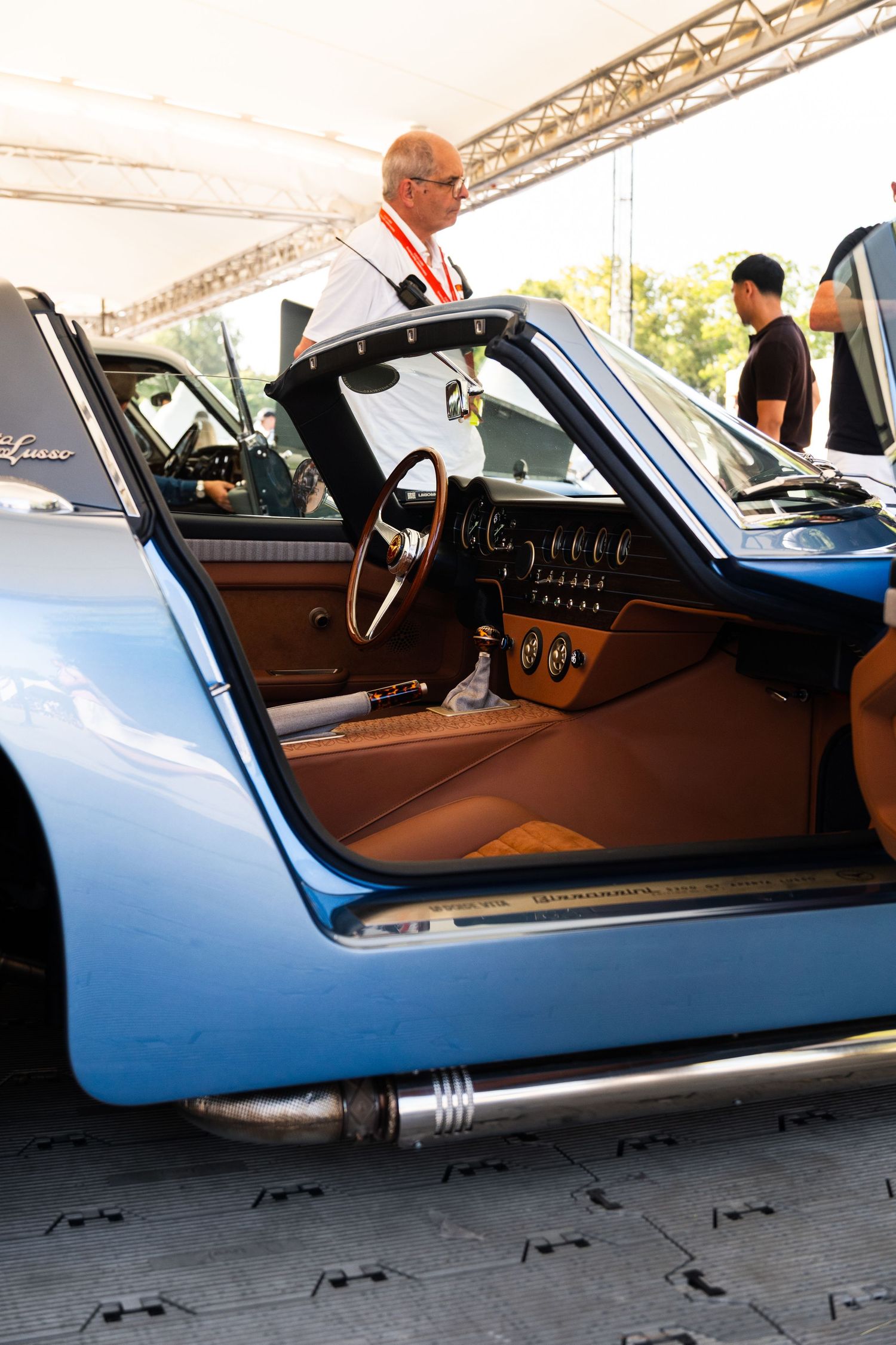 Classic blue sports car with open door revealing tan leather interior and wood steering wheel at vintage auto show.