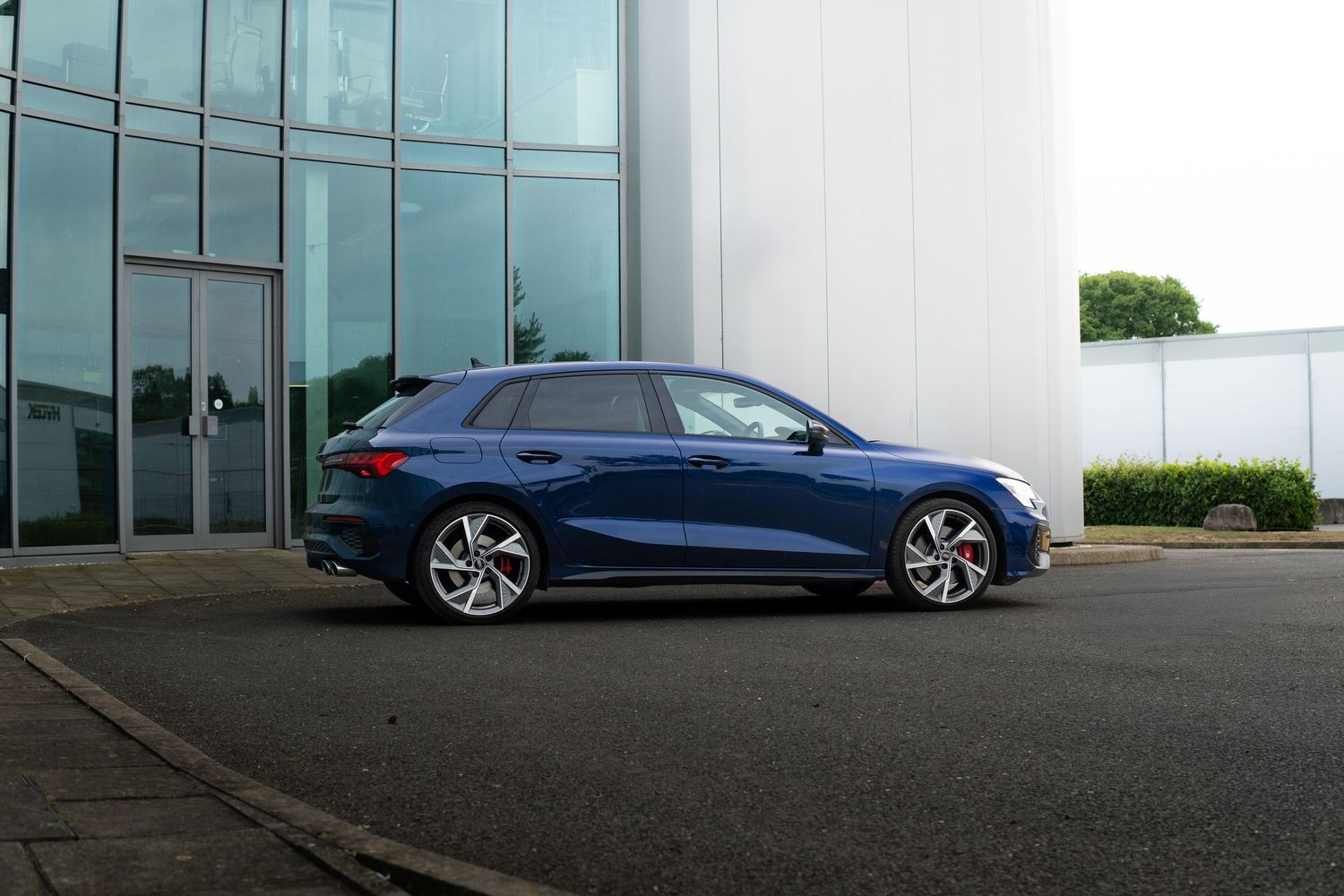 Side profile of a navy blue Audi S3 Sportback parked outside a contemporary building.