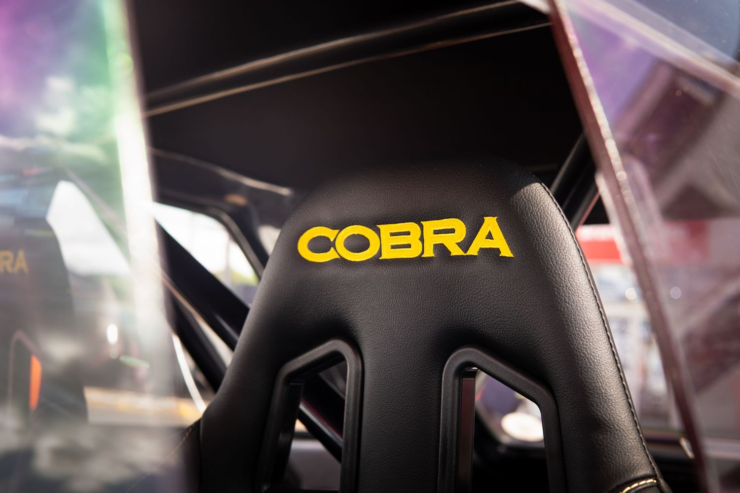 Black Cobra racing bucket seat with yellow logo inside a competition car cockpit.