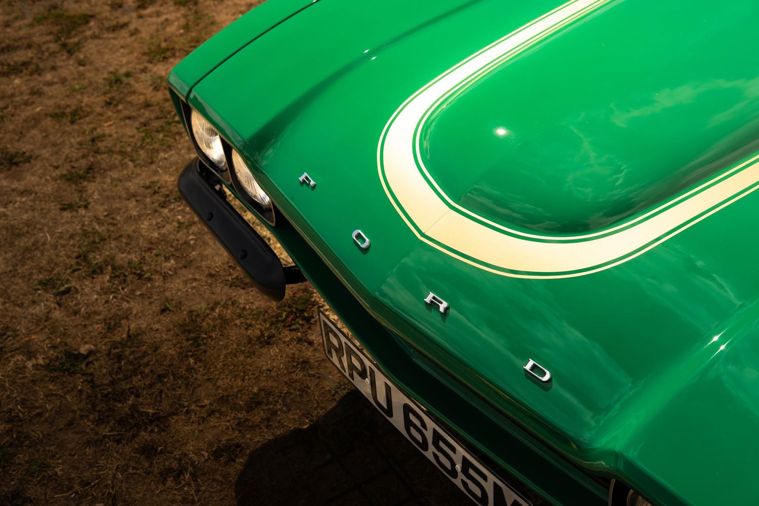 Close-up of a vibrant green Ford classic car hood with white racing stripe and chrome lettering.