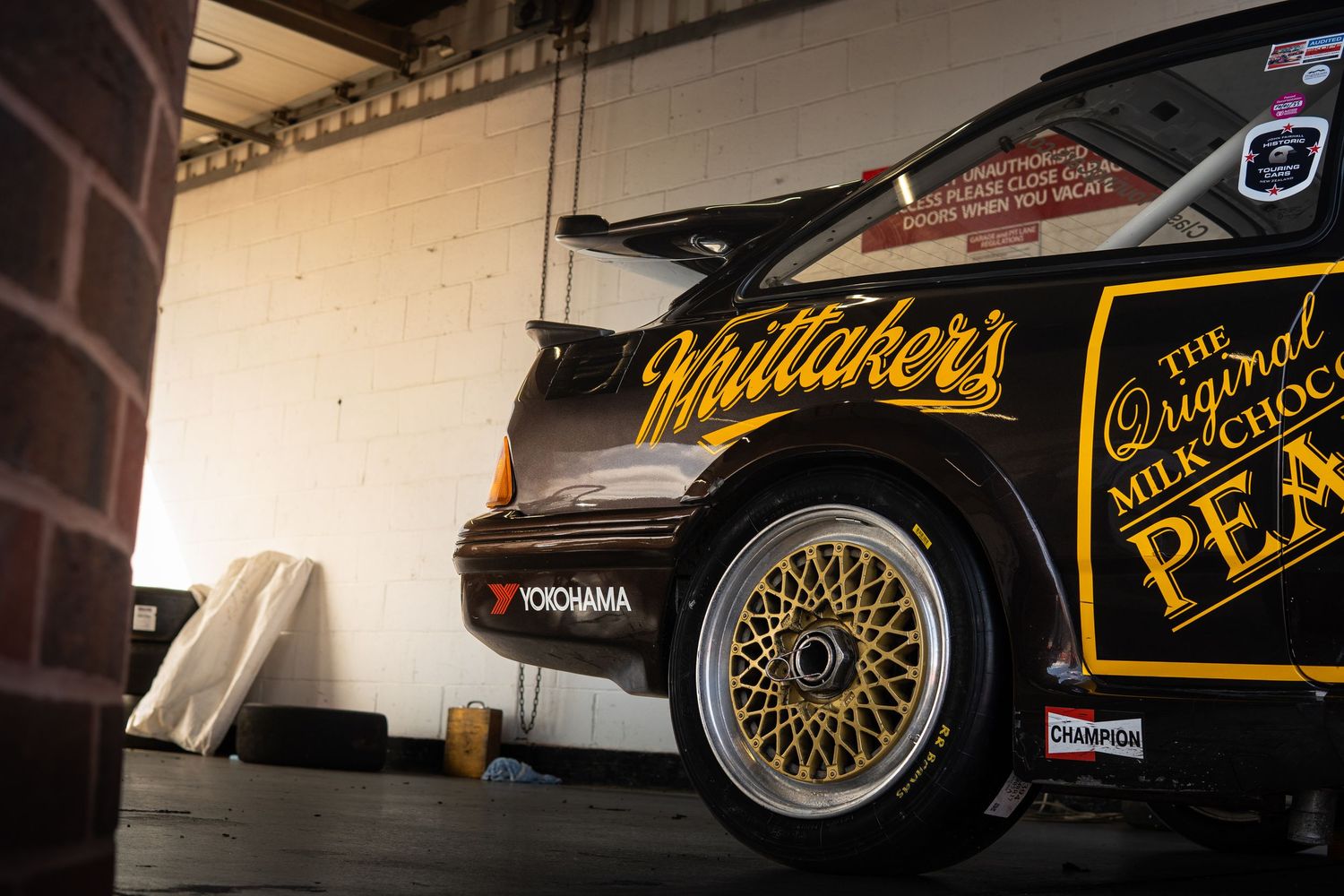 Black Whittakers chocolate sponsored race car with gold BBS wheels in garage.