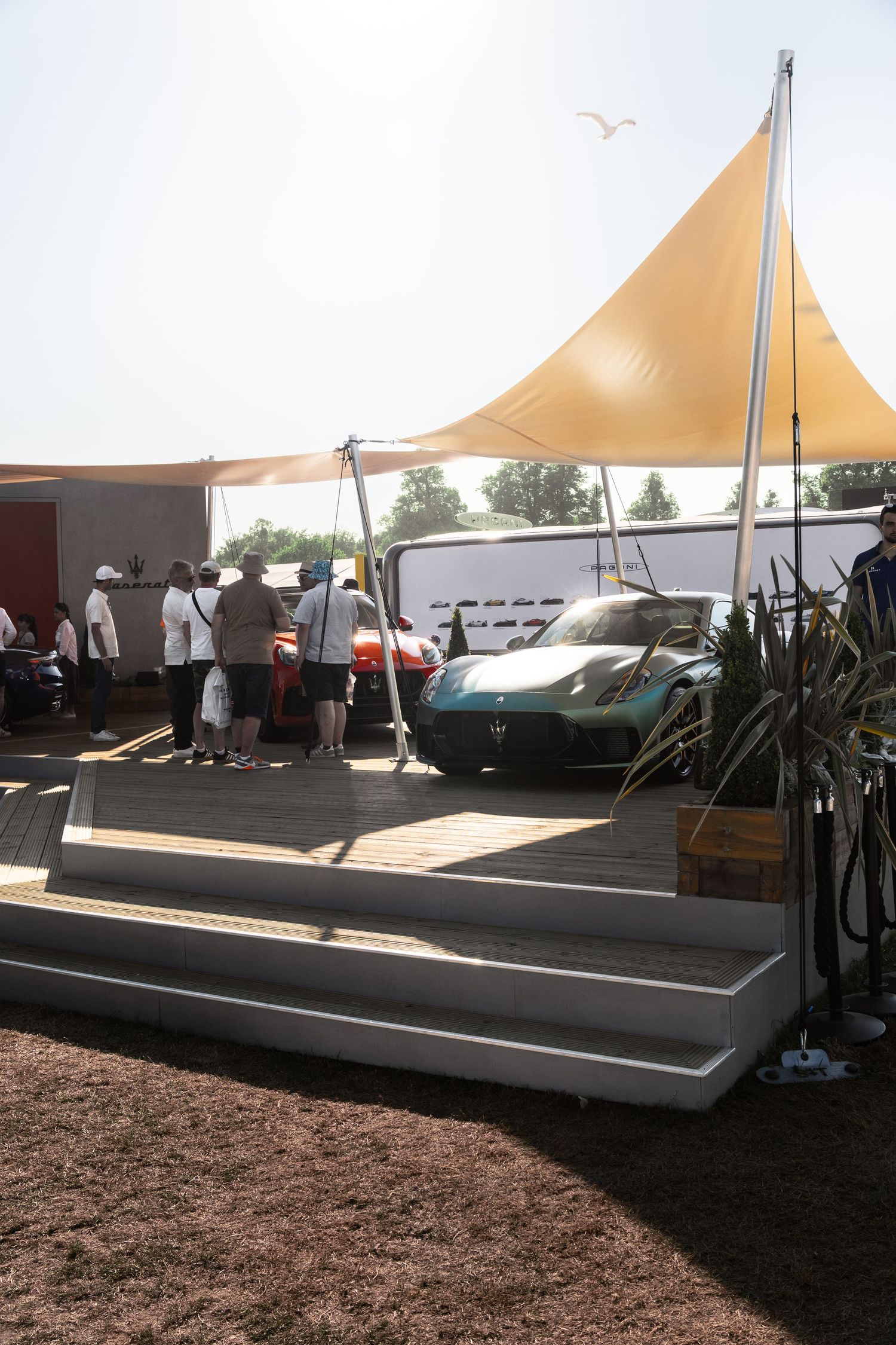Maserati sports car on display at outdoor automotive show with yellow canopy shade structure and spectators.