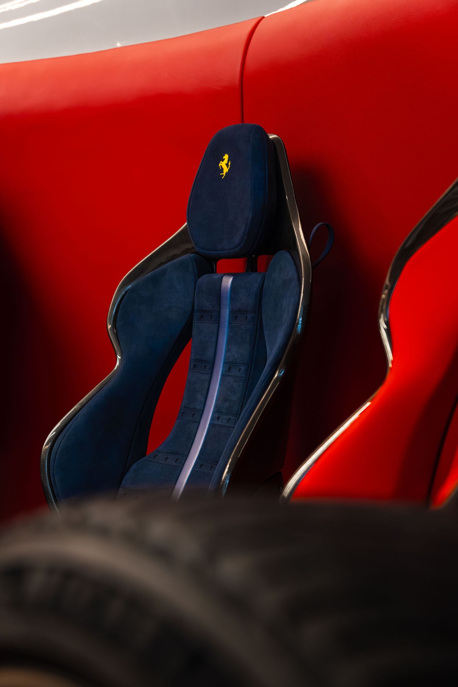 Ferrari racing seat in blue suede with yellow prancing horse logo against a red car body.