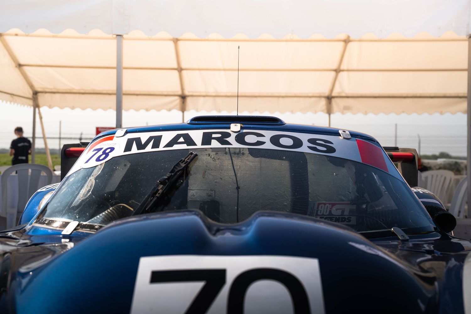 Marcos racing car number 78 seen from behind at a motorsport circuit paddock area.