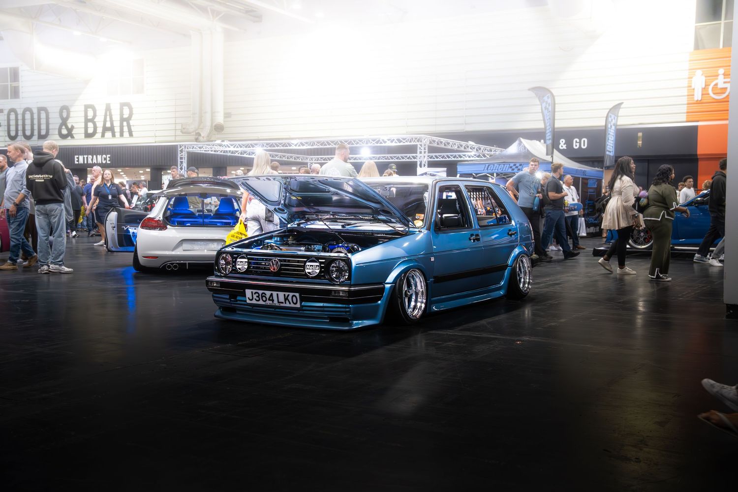 Teal blue lowered VW Golf Mk2 on air suspension at indoor automotive car show.