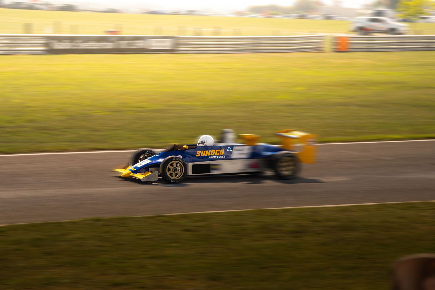 Blue and yellow Formula racing car speeding on track with motion blur background.