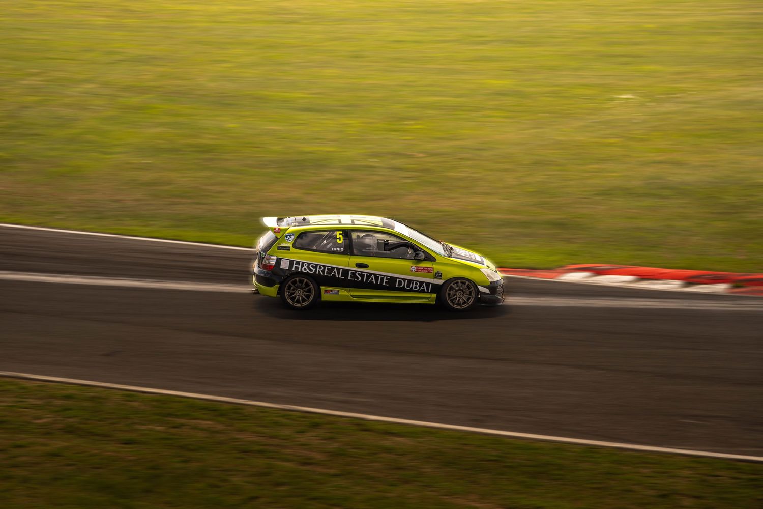 Yellow-green touring car racing at speed on a motorsport circuit at dusk.