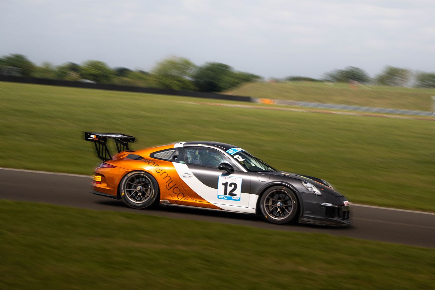 Porsche GT3 Cup number 12 in orange livery racing on a track.