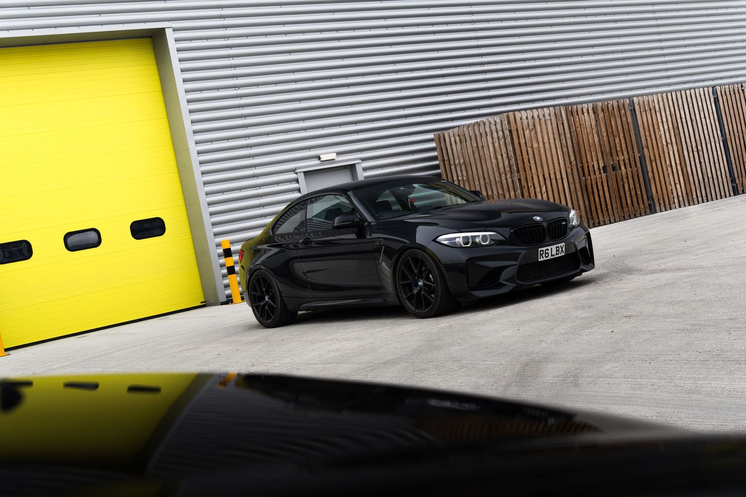 Black BMW M2 coupe parked at an angle in front of yellow garage doors.