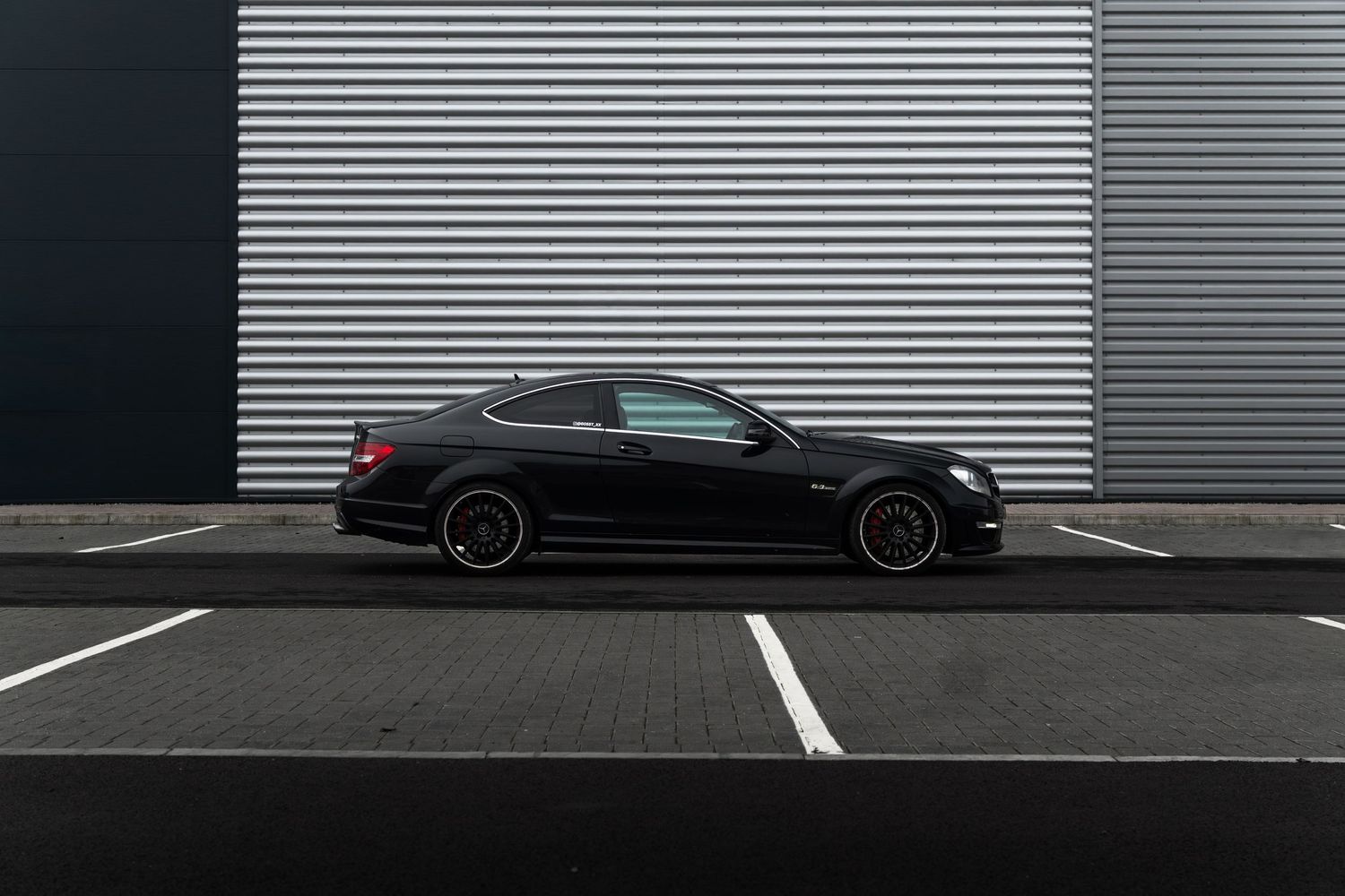 Sleek black Mercedes-Benz C-Class coupe parked in lot against corrugated metal wall.