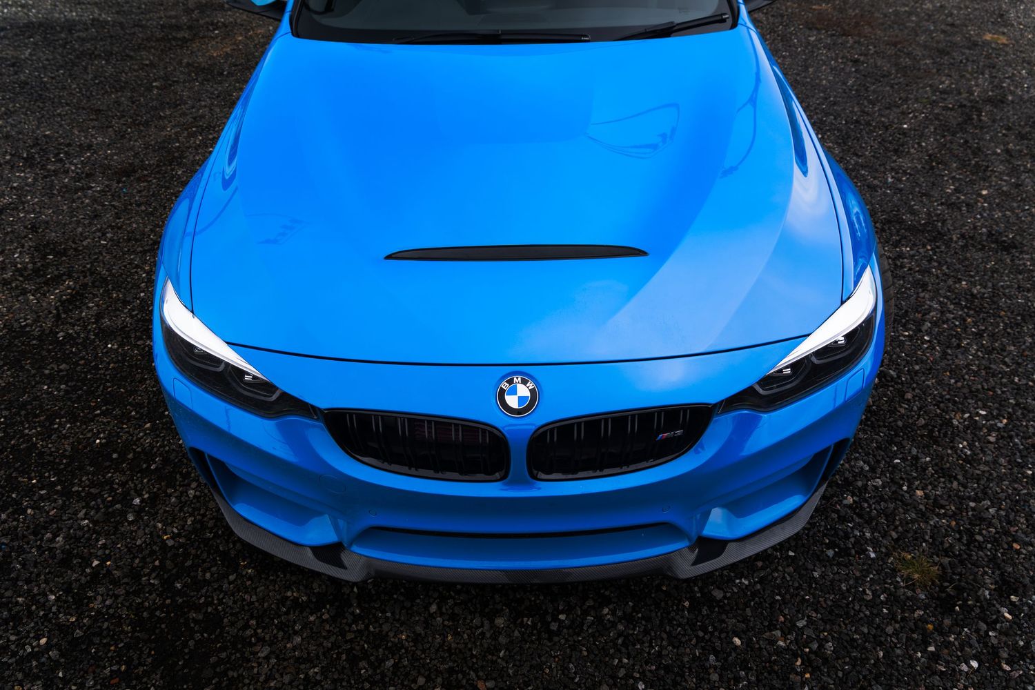 Overhead view of a blue BMW M4 with carbon hood scoop and kidney grille.