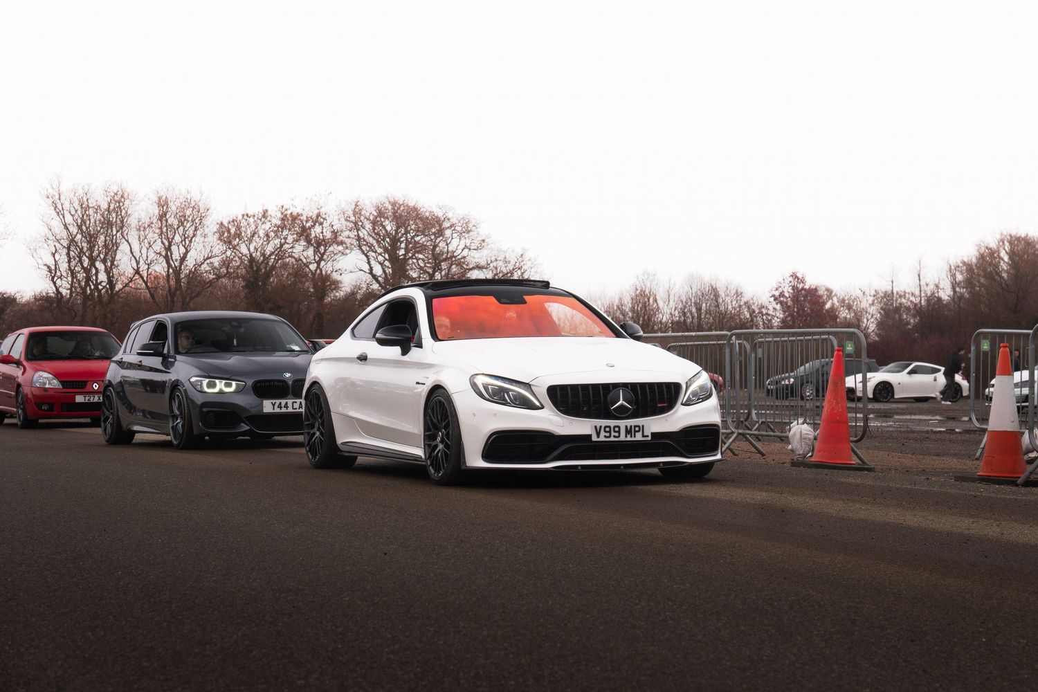 White Mercedes-AMG C63 coupe leads a line of cars at a track day event.