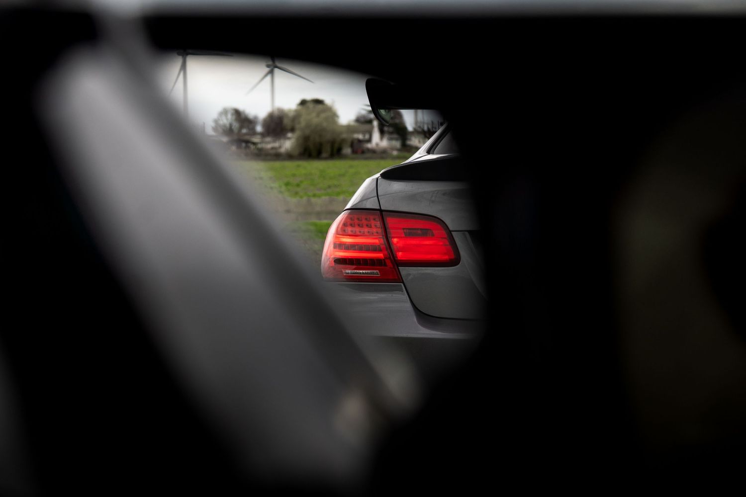 Close-up view of a silver BMW M3 tail light framed through a car window opening.