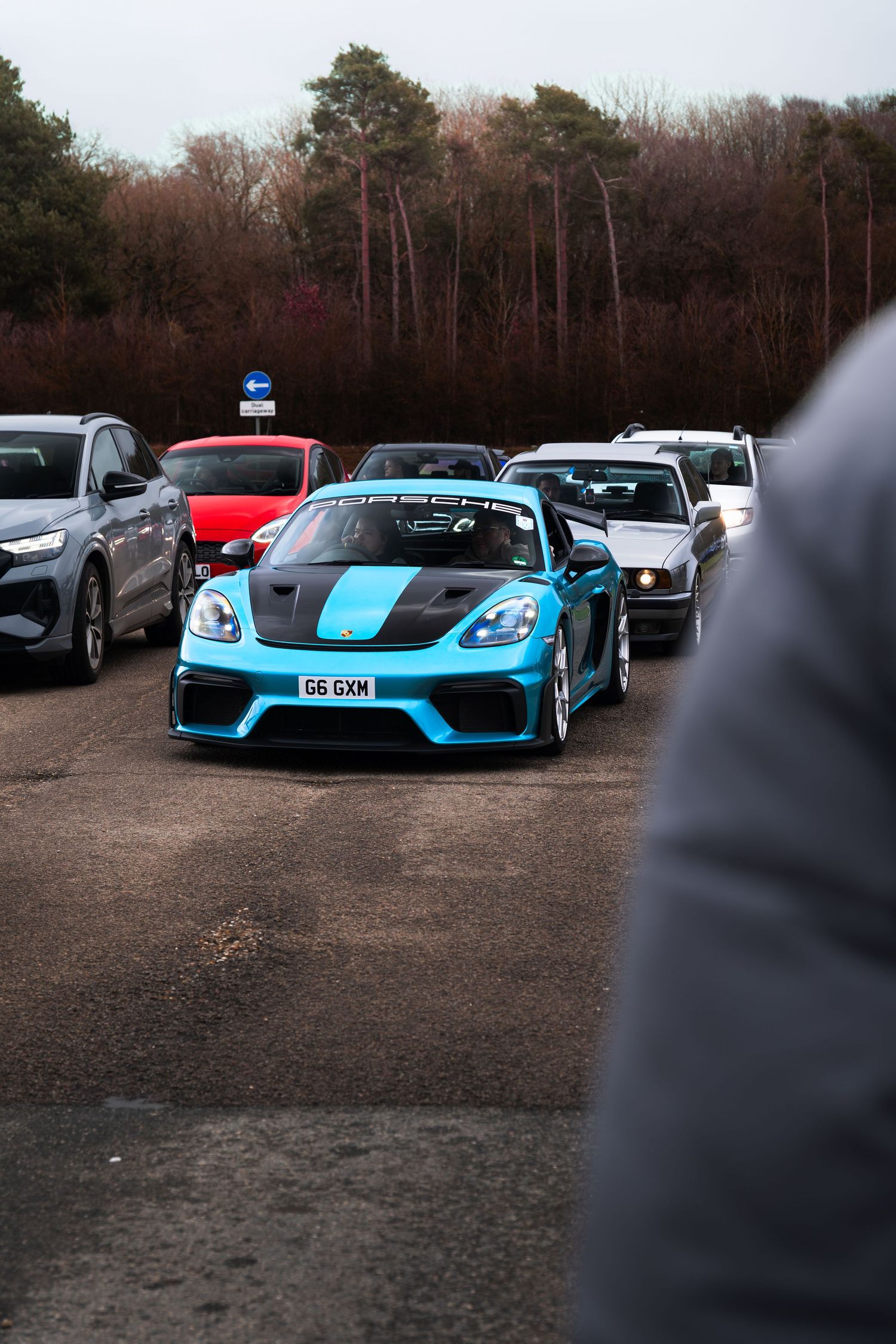Blue Porsche 718 Cayman GT4 with racing stripe at a UK car meet event.