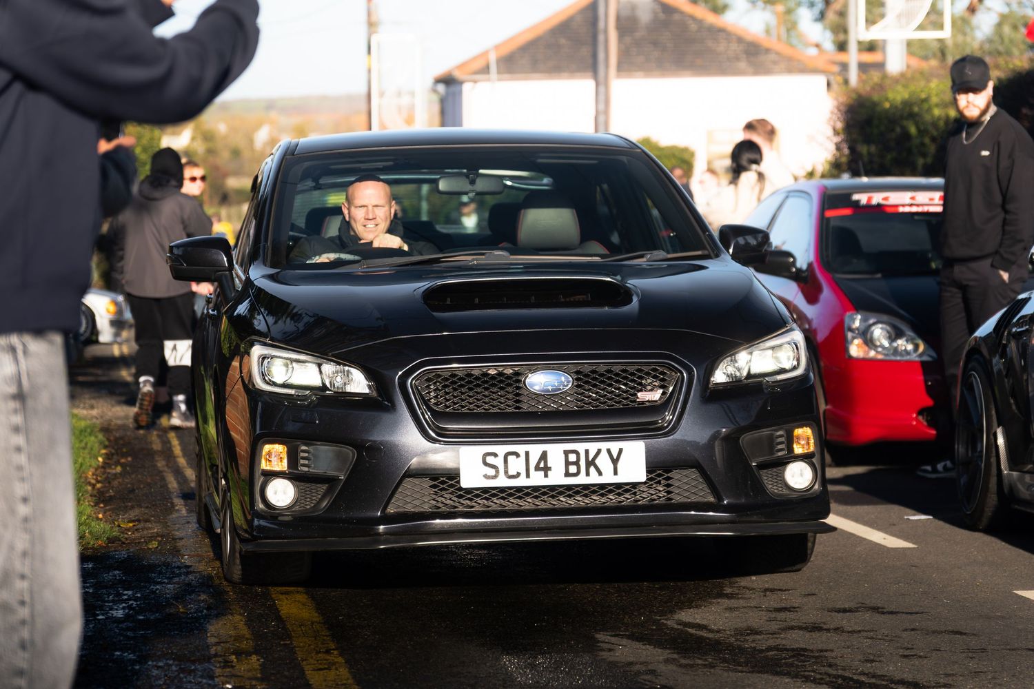 Black Subaru WRX STI with smiling driver at a UK car meet event.