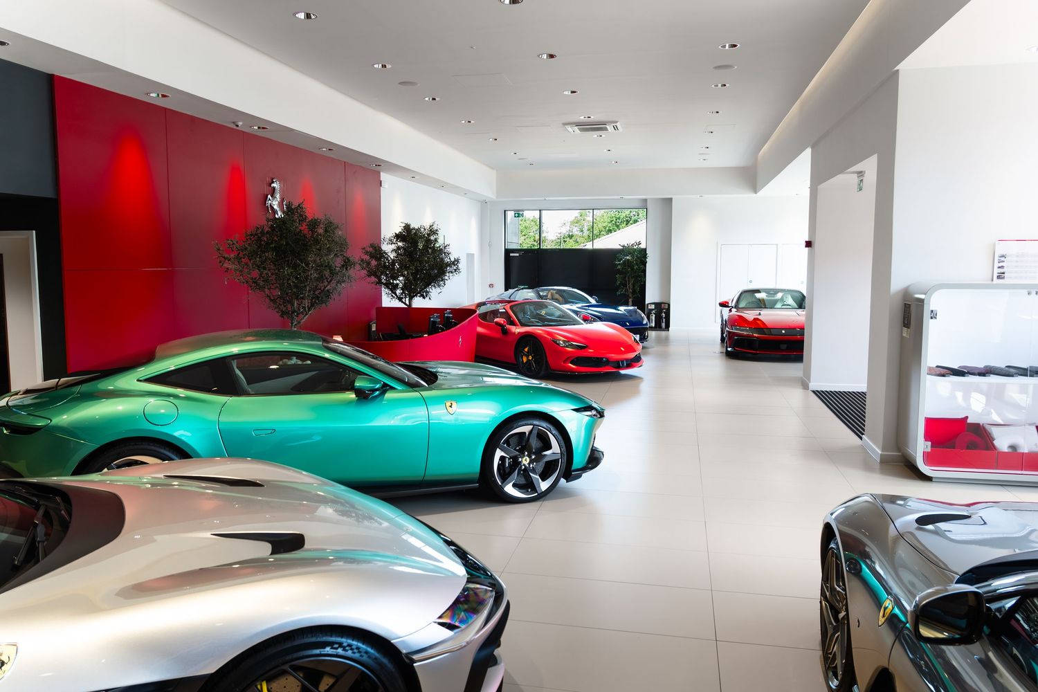 Luxury Ferrari showroom displaying multiple exotic sports cars including teal and red models on a polished white floor.