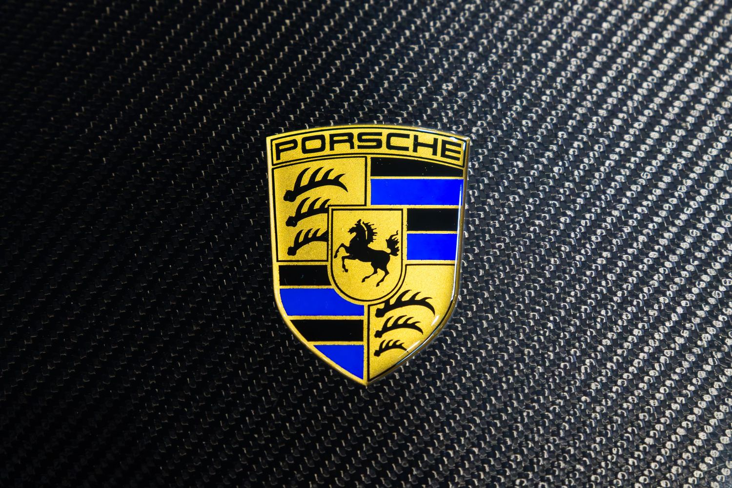 Porsche crest badge logo on carbon fiber background, gold and blue shield emblem closeup.