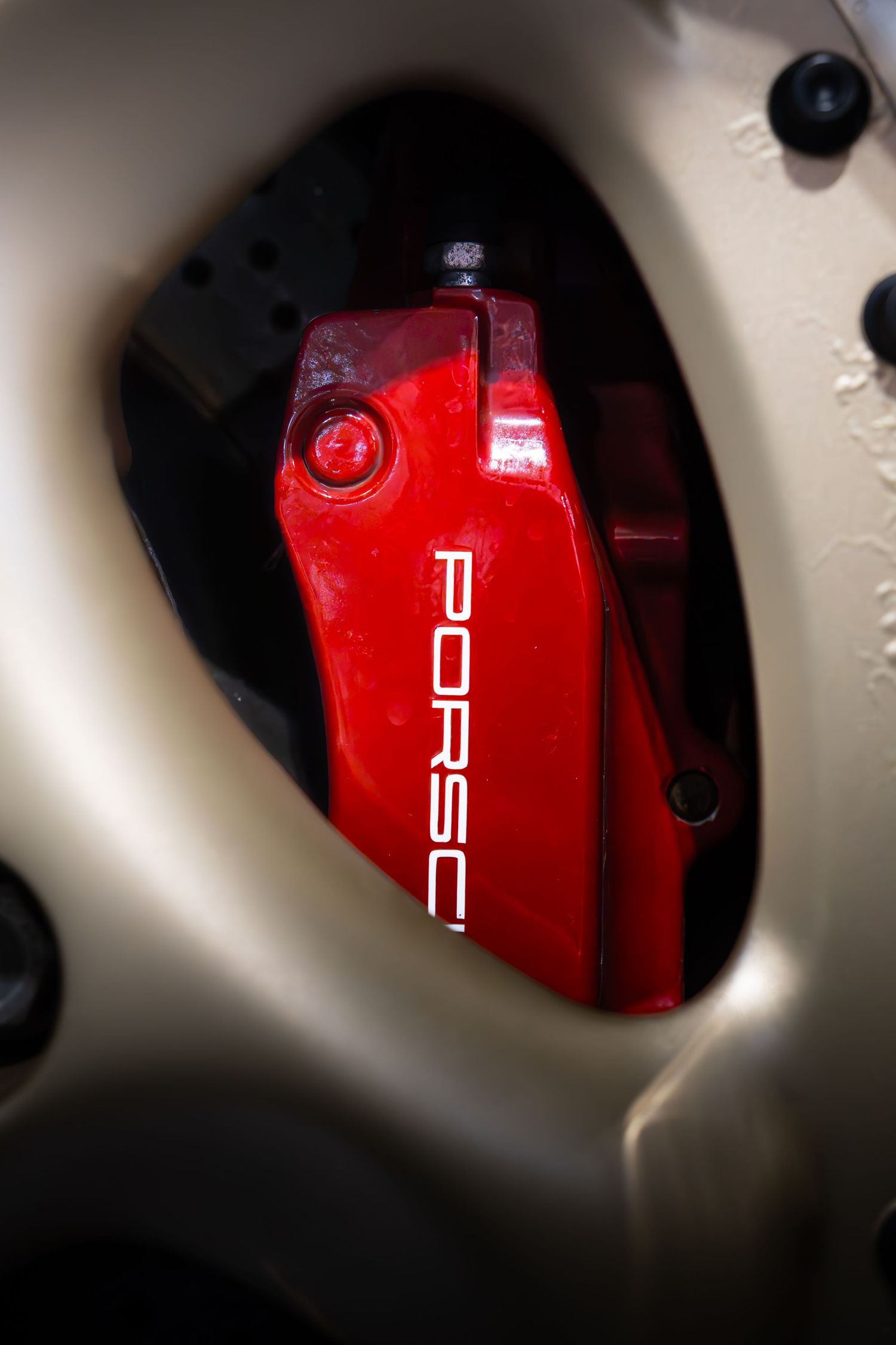 Red Porsche brake caliper visible through gold alloy wheel spoke on a sports car.