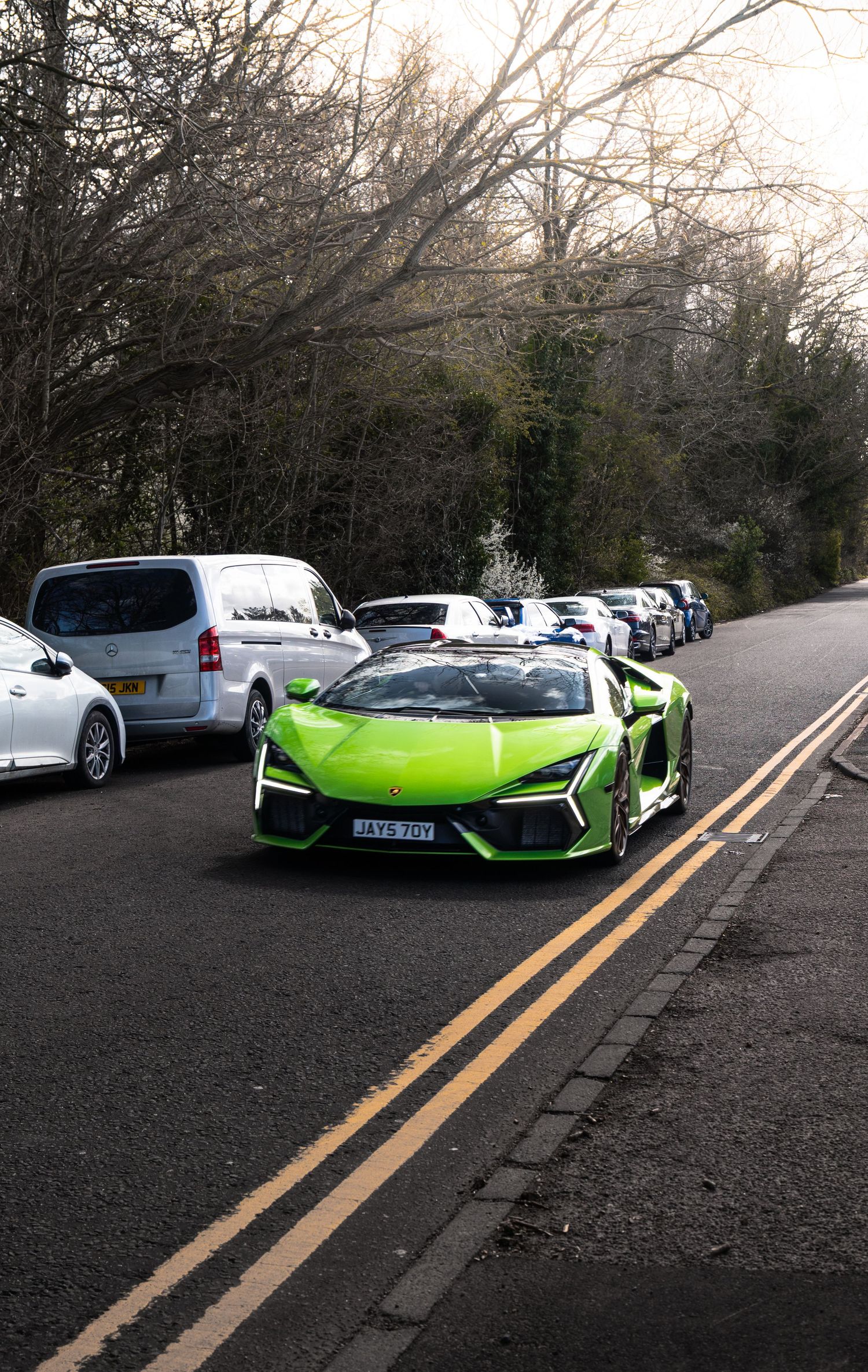 Lime green Lamborghini Revuelto supercar driving on a tree-lined road.