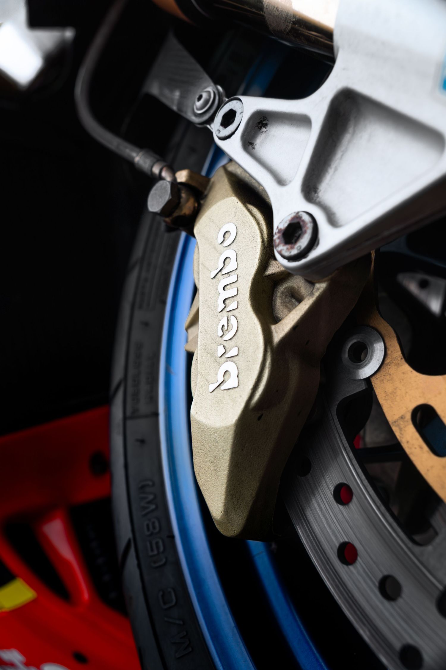 Close-up of a gold Brembo brake caliper on a motorcycle wheel with blue rim and drilled disc.