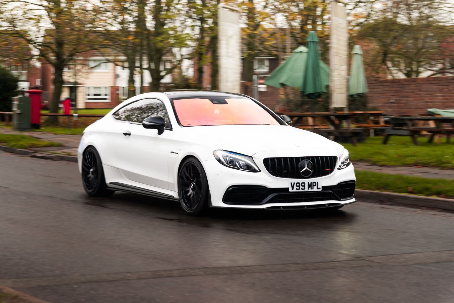 White Mercedes-AMG C63 Coupe driving on wet suburban road.
