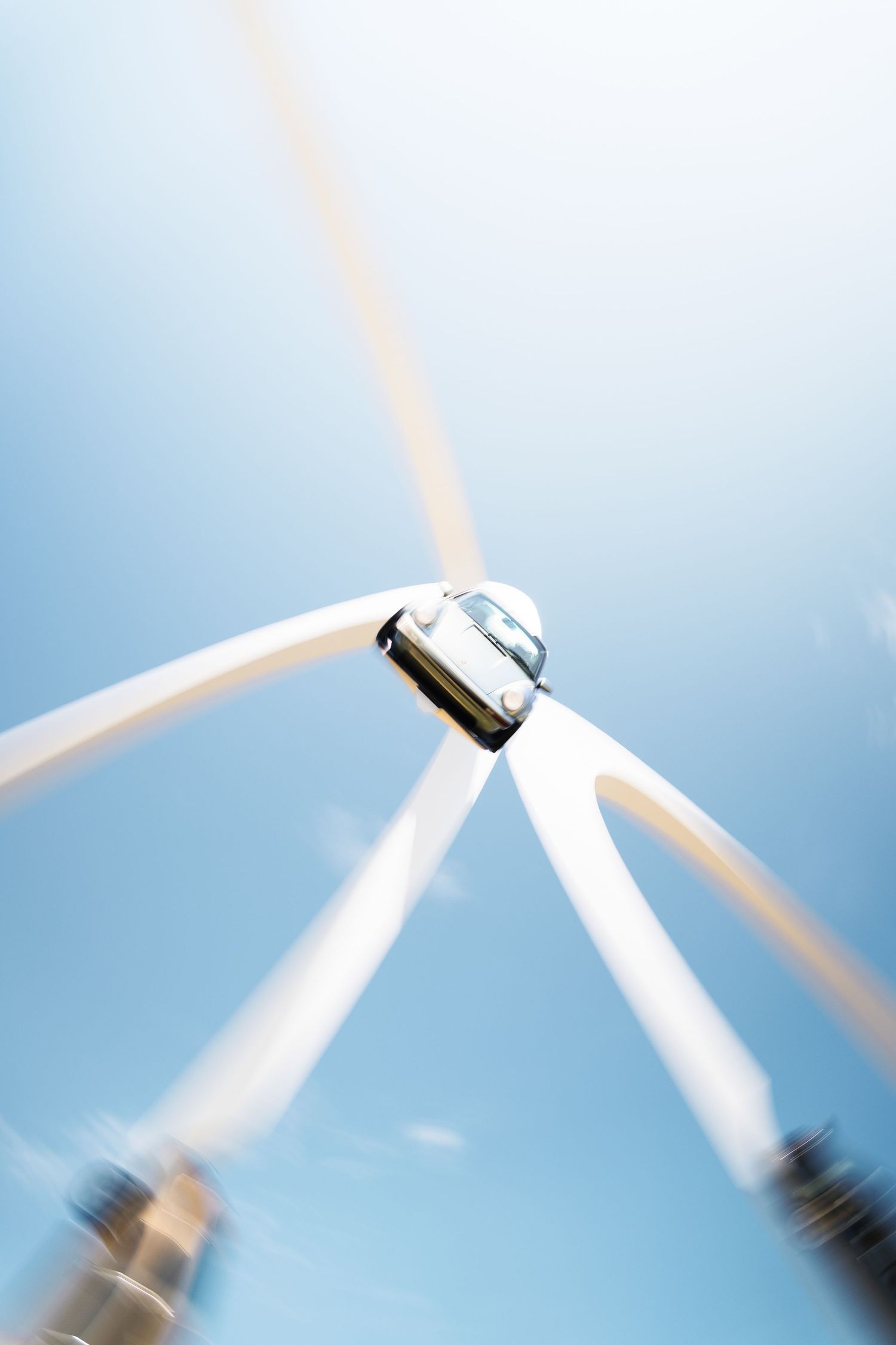 Low-angle view of a spinning wind turbine against a clear blue sky, captured with motion blur on the blades.