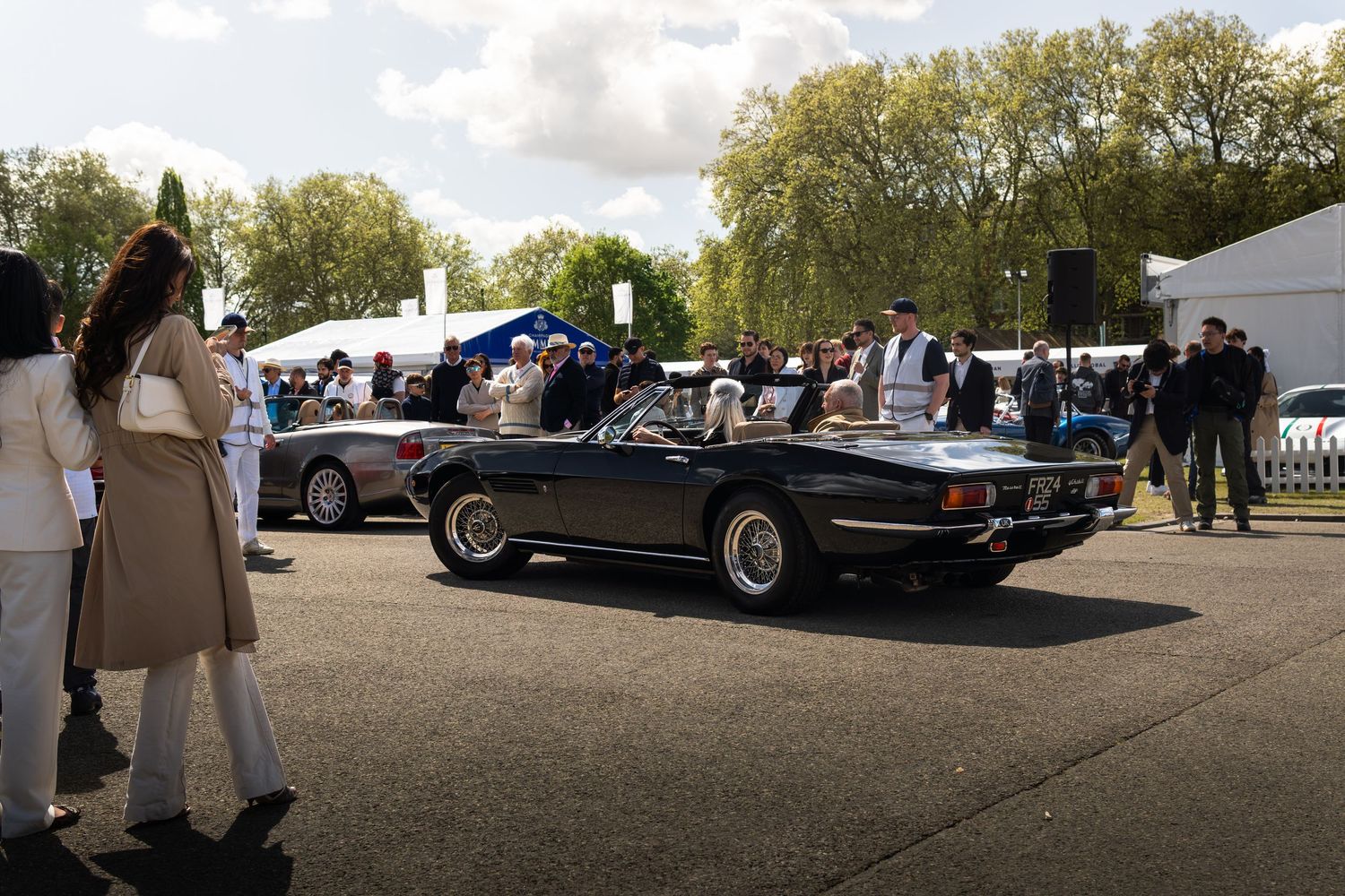 Classic black convertible sports car on display at an outdoor automotive concours event with crowds gathered.