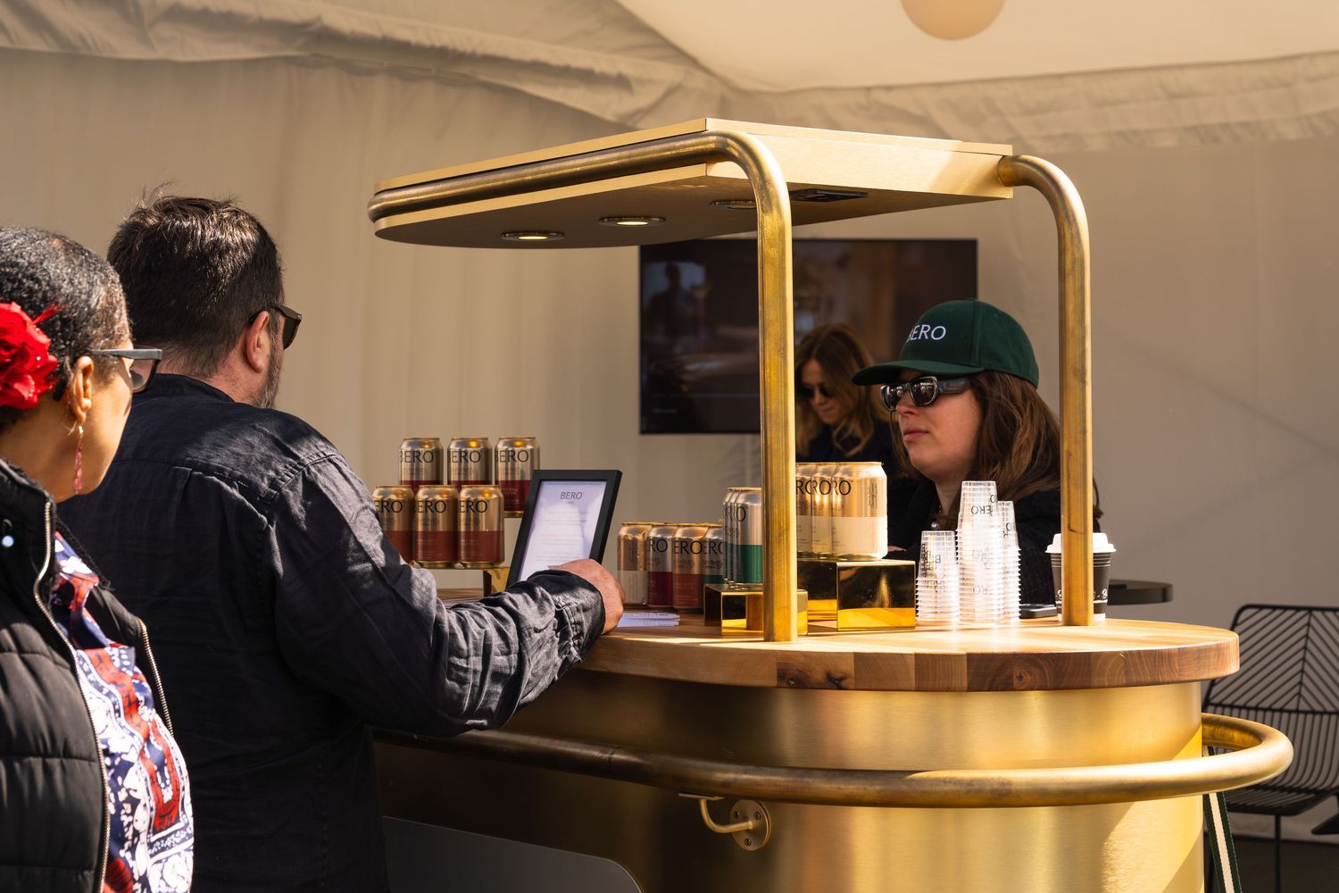 Customers ordering at a stylish gold circular bar kiosk at an outdoor food and drink festival event.