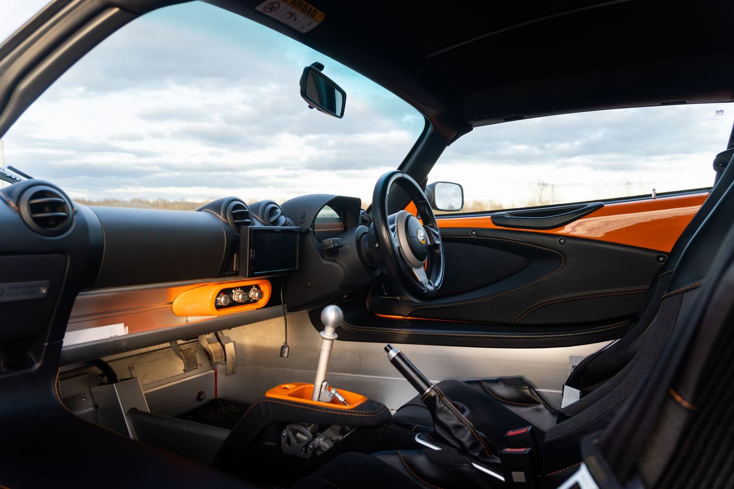 Orange and black Lotus Elise interior showing manual gearshift, sport seats and dashboard detail.