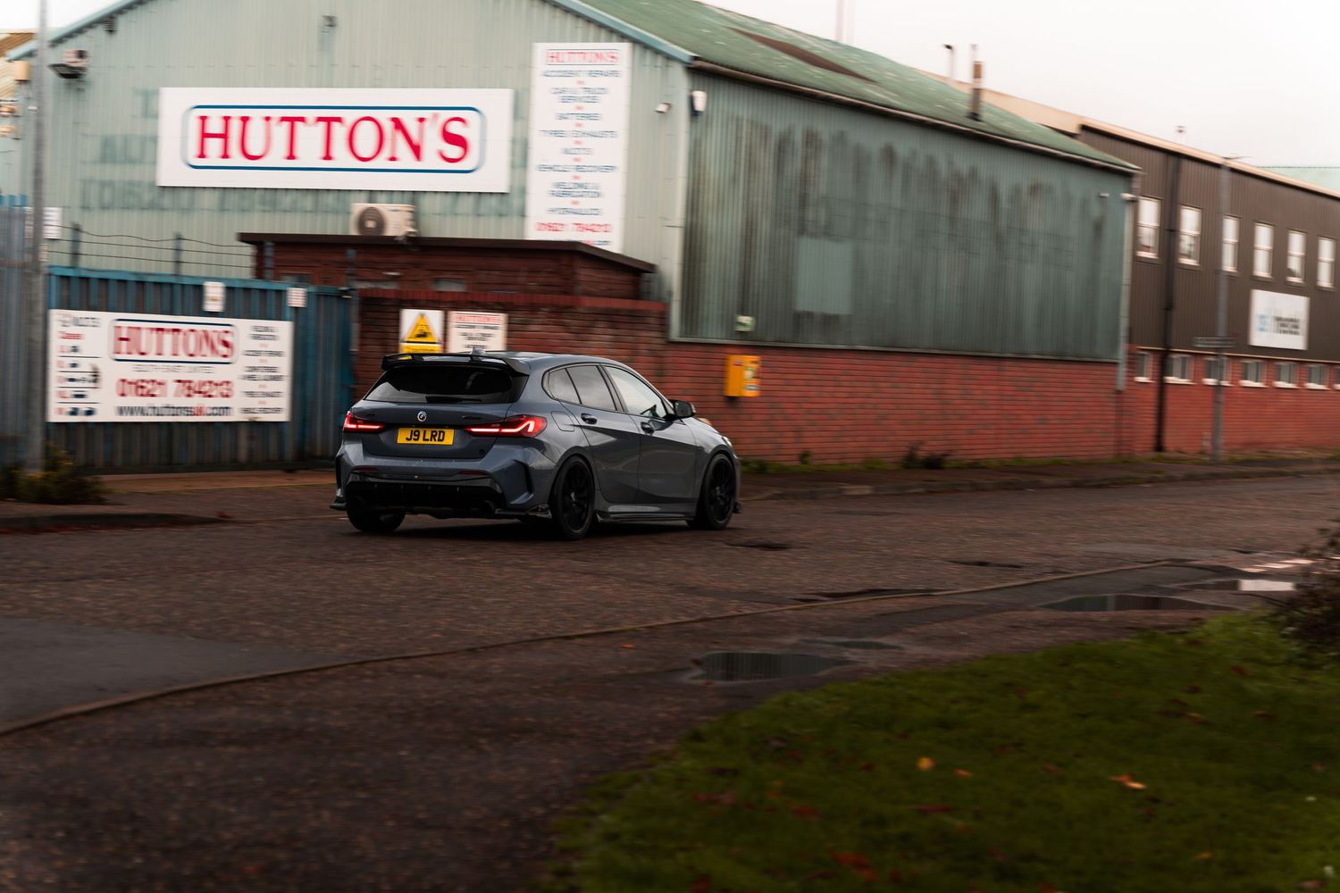 Dark grey BMW 1 Series parked in lot outside Huttons industrial building.