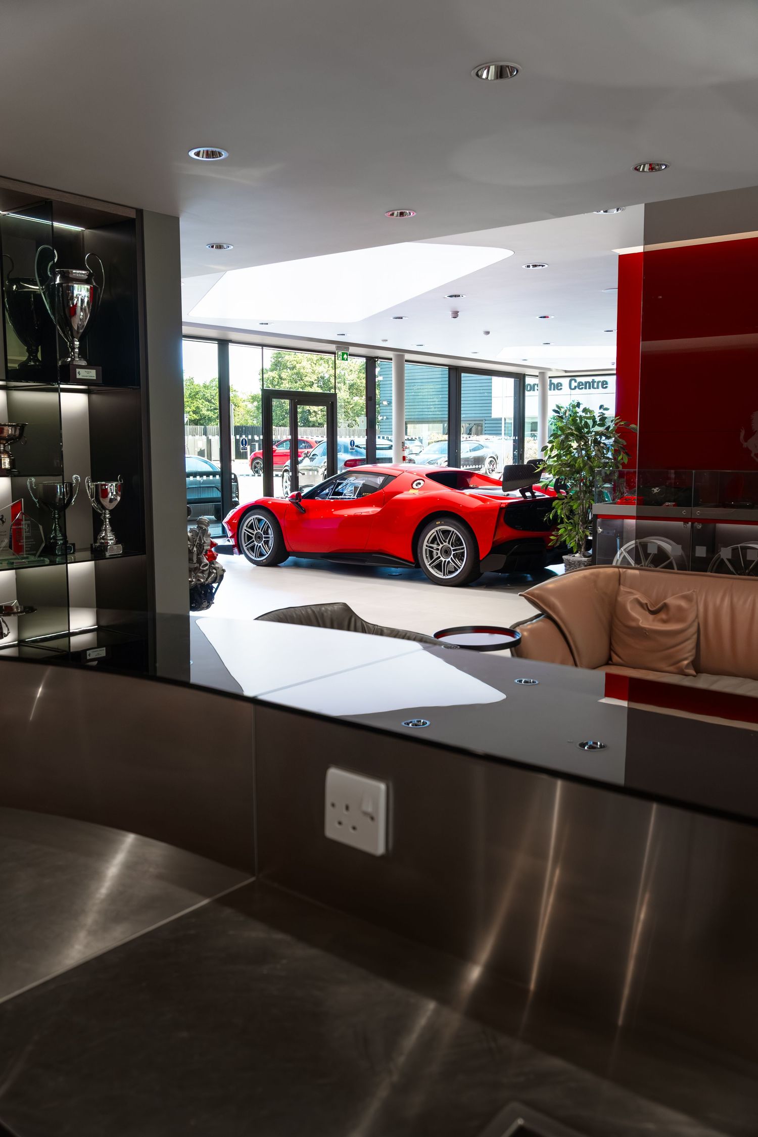 Red Ferrari on display in a luxury car dealership showroom with trophies visible on shelves.