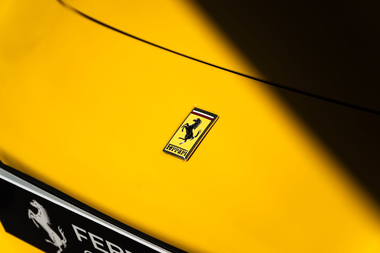 Close-up of a Ferrari prancing horse logo badge on a vibrant yellow Ferrari sports car hood.