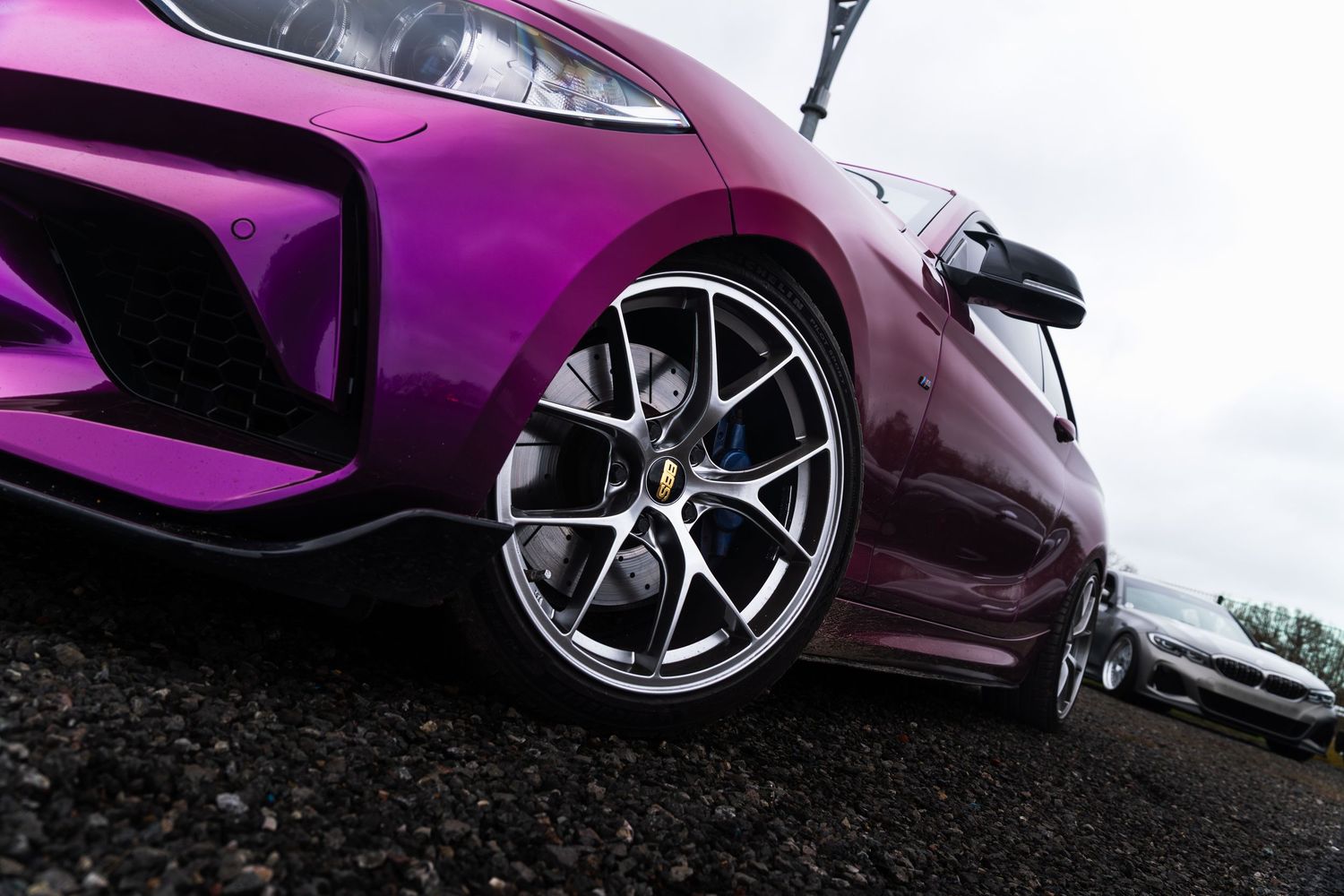 Close-up of a purple sports car's alloy wheel and front bumper at a car show.