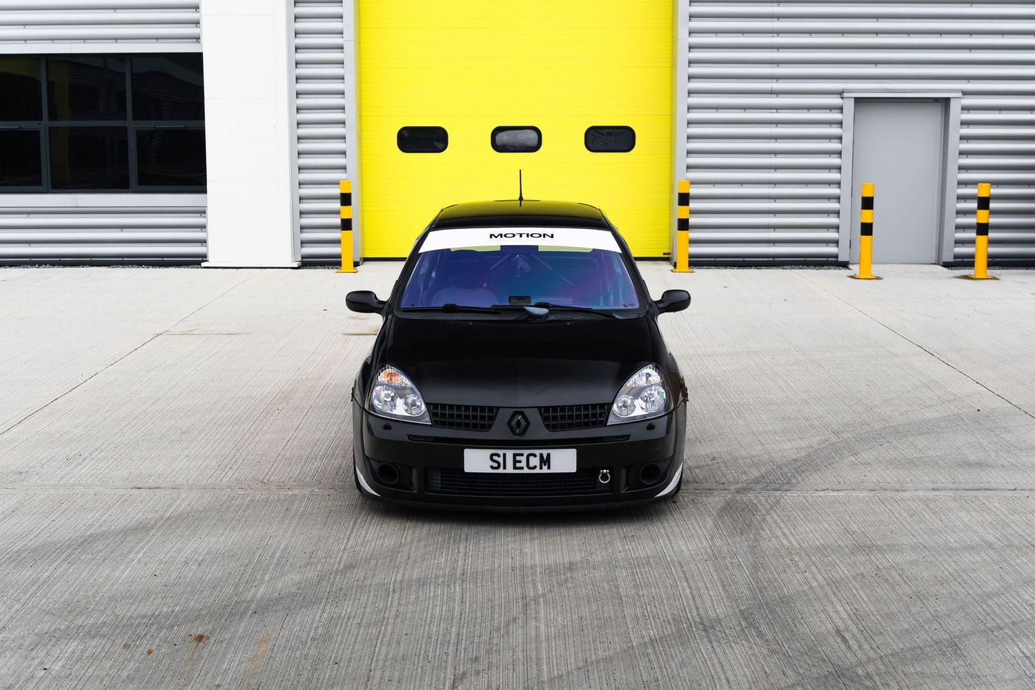 Front view of a black Renault Clio with Motion windscreen banner outside yellow garage doors.
