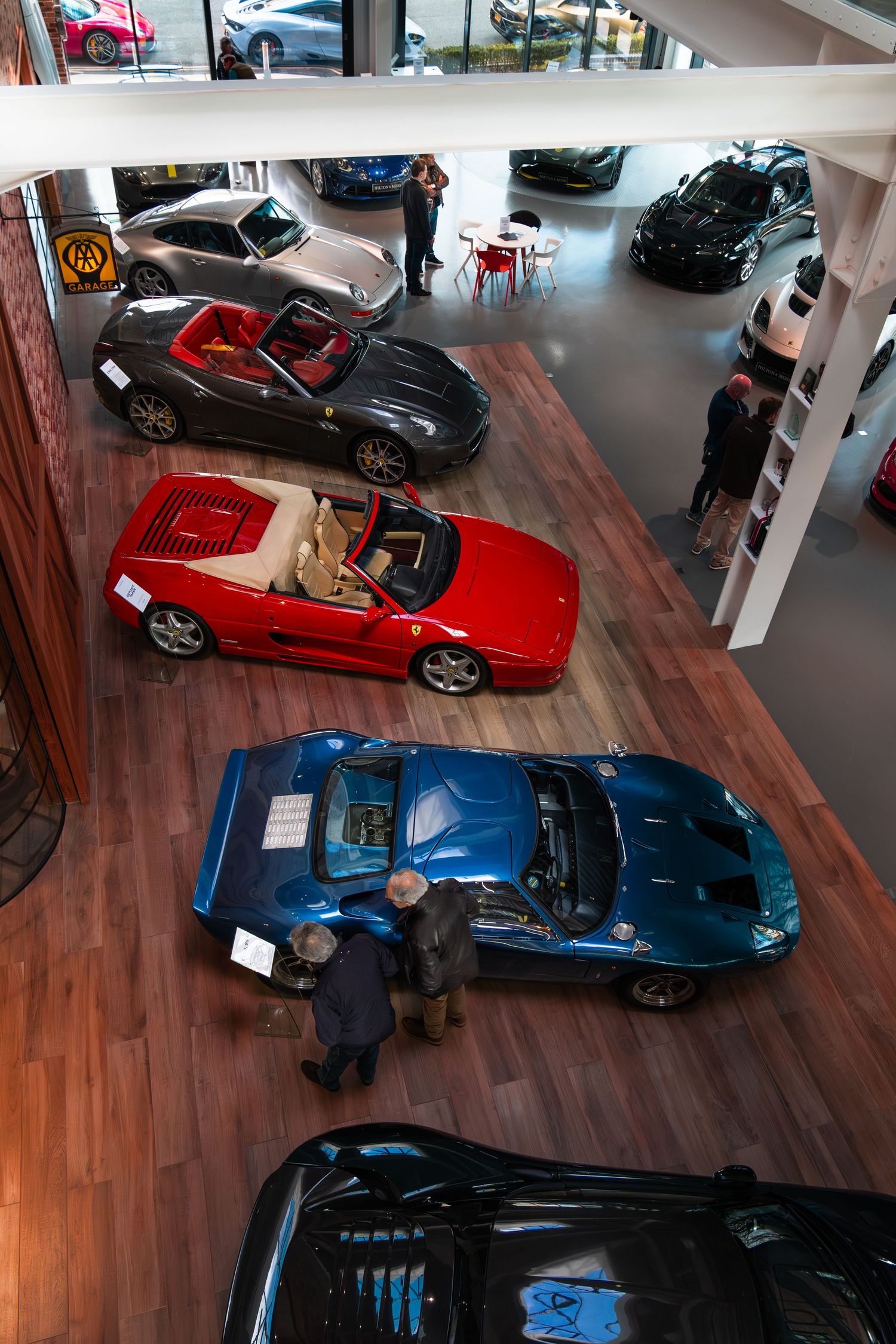 Overhead view of luxury car showroom featuring blue supercar, red Ferrari convertible, and grey sports cars.