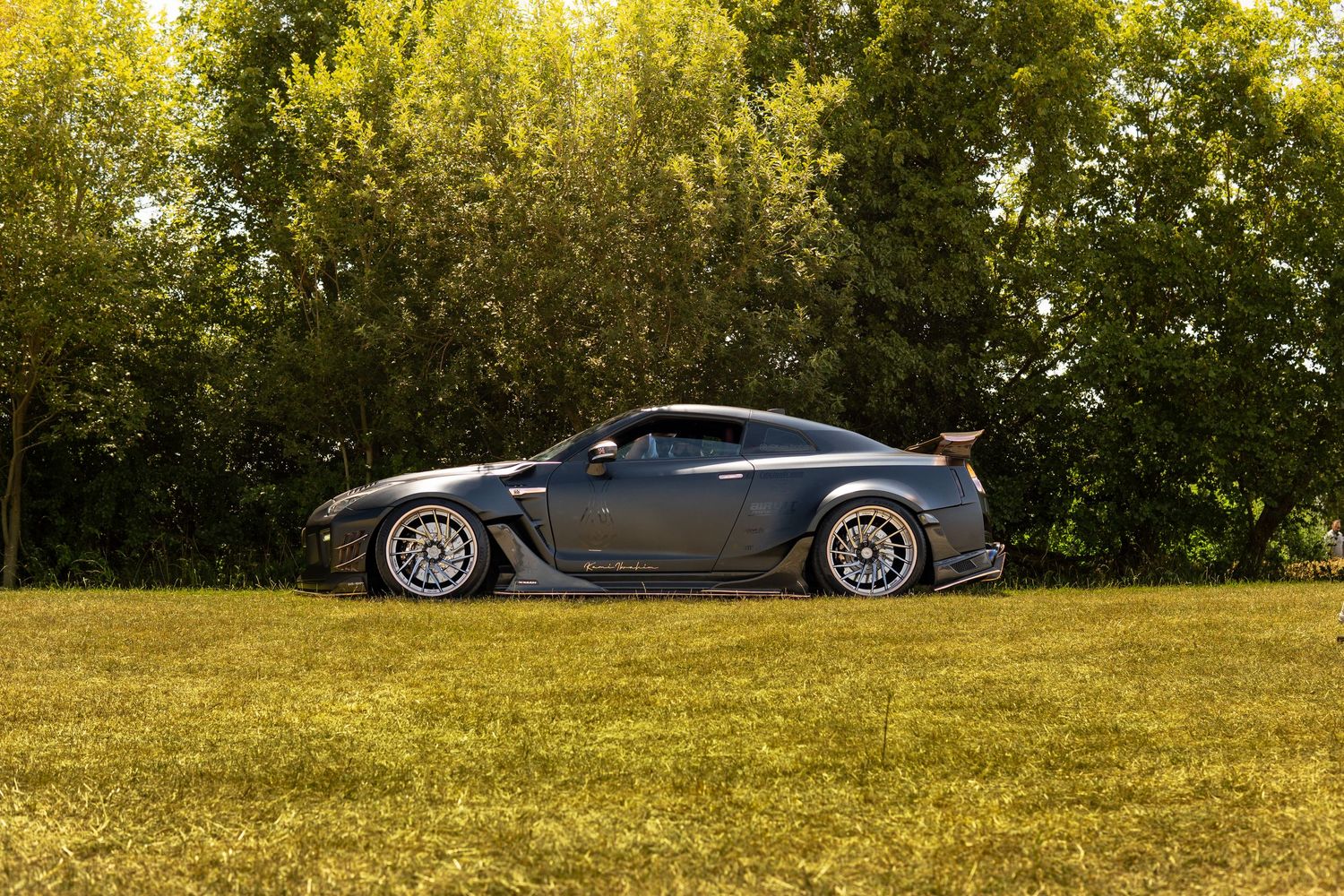 Side profile of modified Nissan GT-R with wide body kit on green grass.