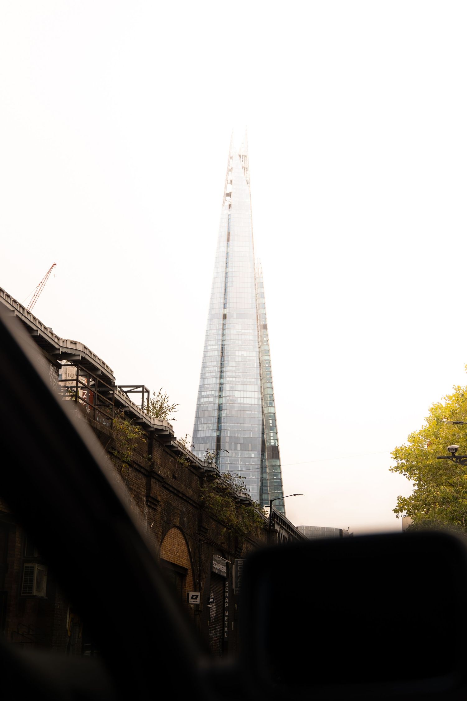 A view of The Shard skyscraper in London rising above railway arches on an overcast day.