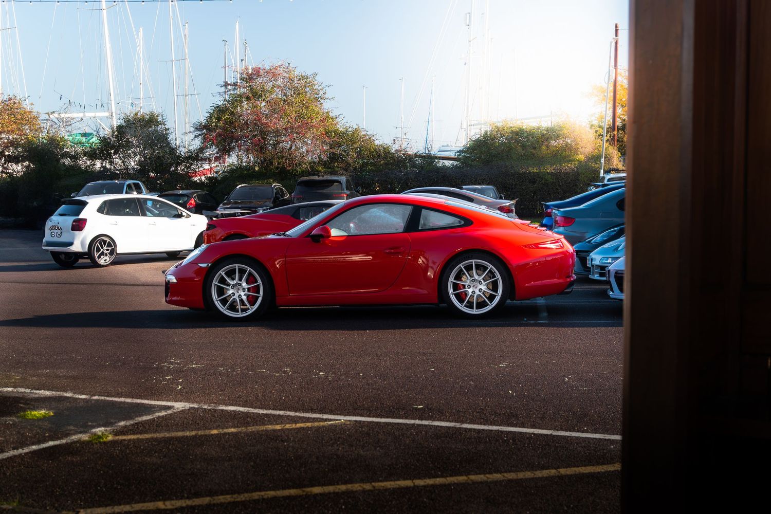 Red Porsche 911 Carrera coupe parked in a marina car park during golden hour.