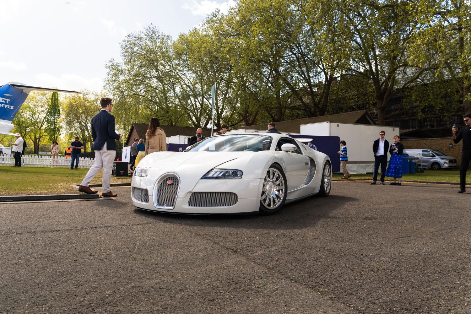 A white Bugatti Veyron luxury supercar on display at an outdoor car show with spectators nearby.